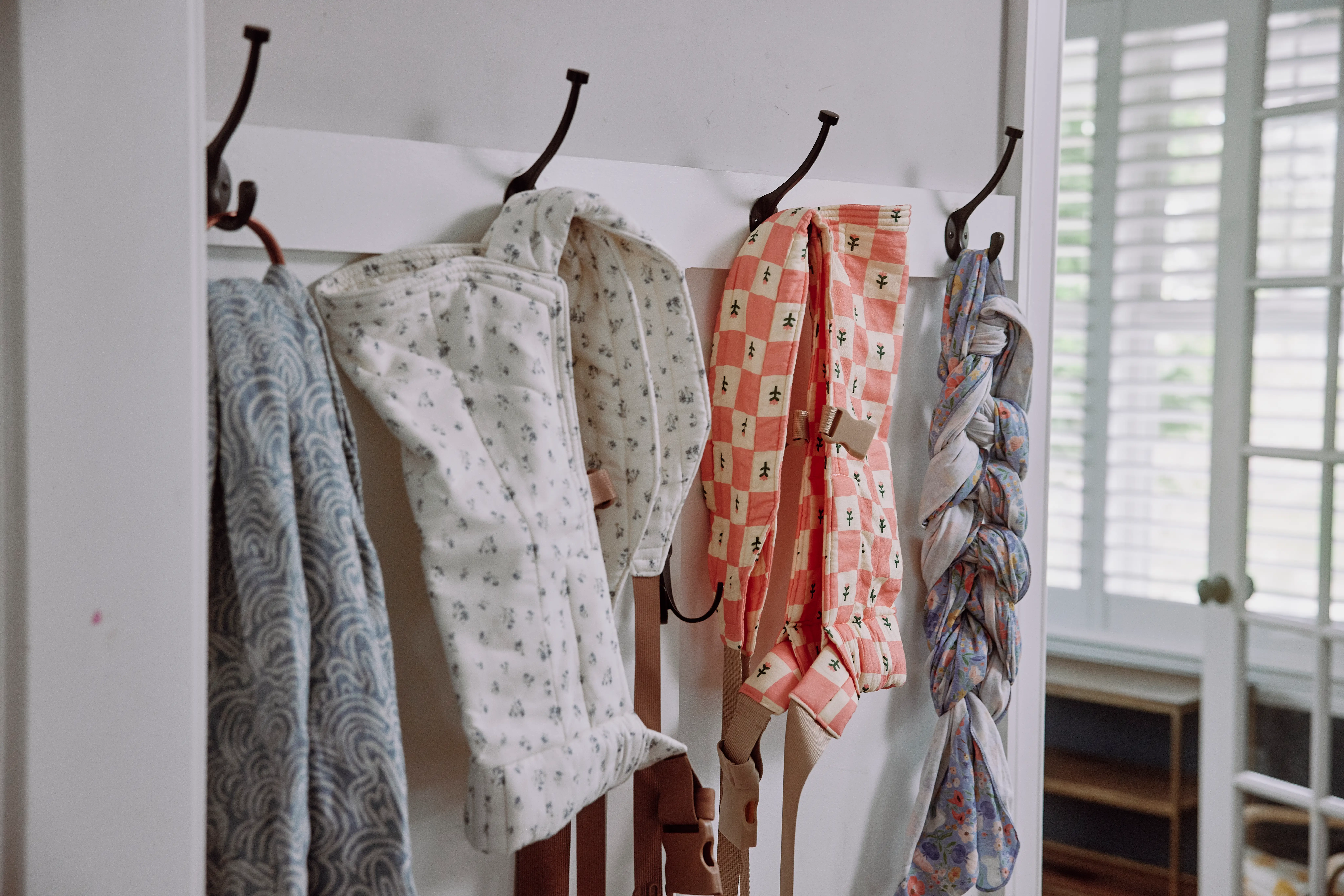 An arrangement of baby carriers, including their buckle baby carrier, in Skye's home.