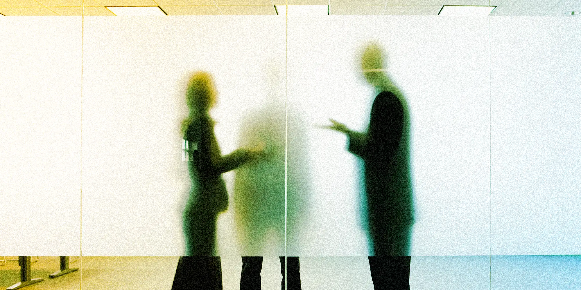 A photo of three business people speaking behind a foggy glassy door