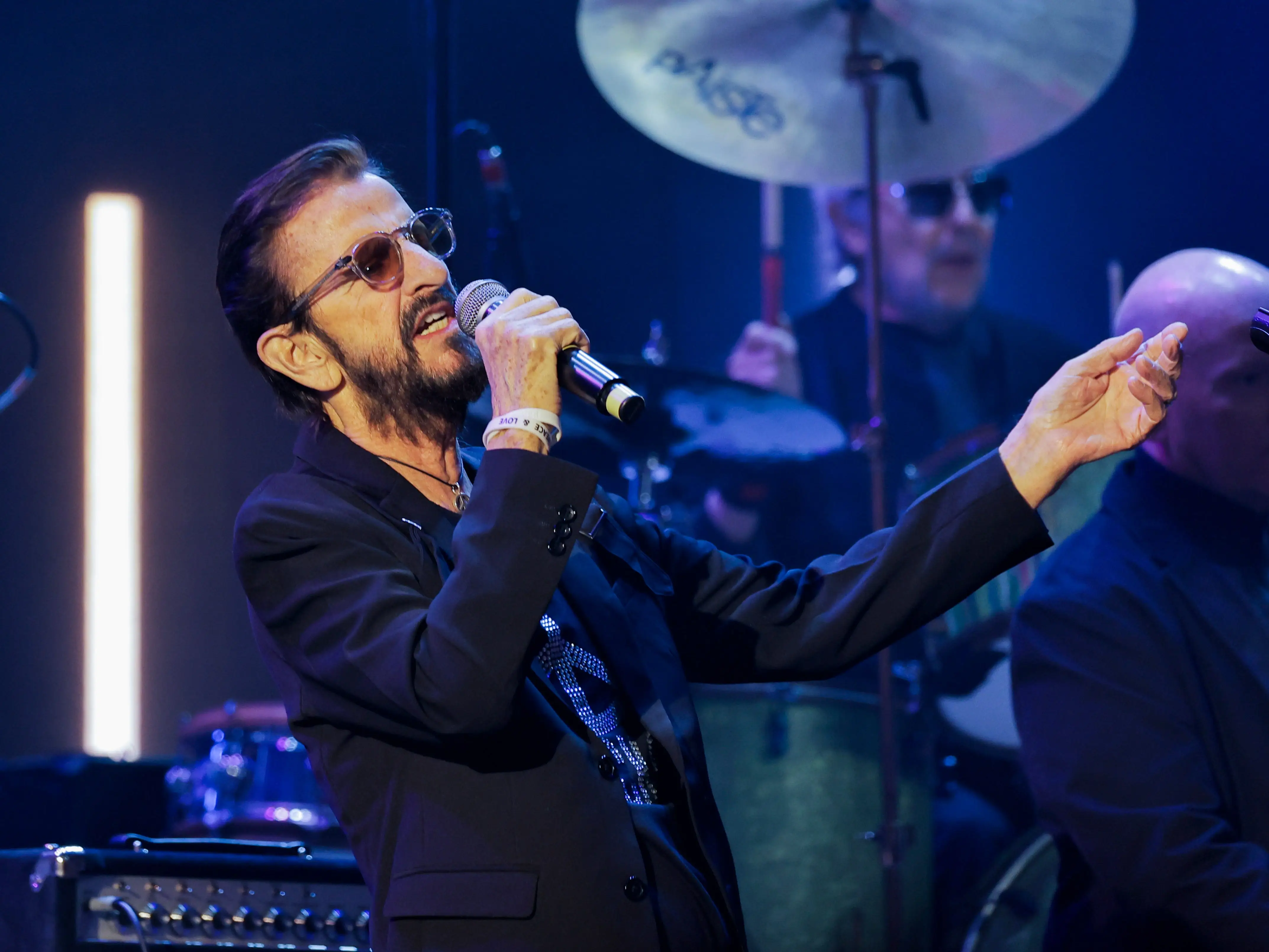 Ringo Starr holding a microphone and singing.