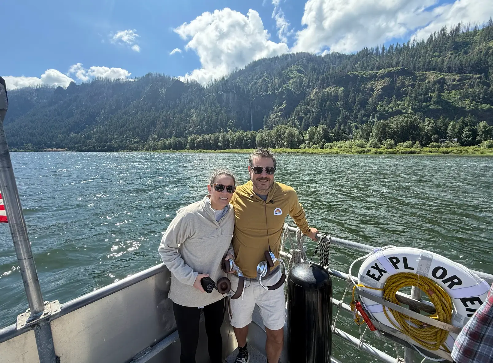 The writer and his wife standing on a boat in Portland, in front of green mountains.
