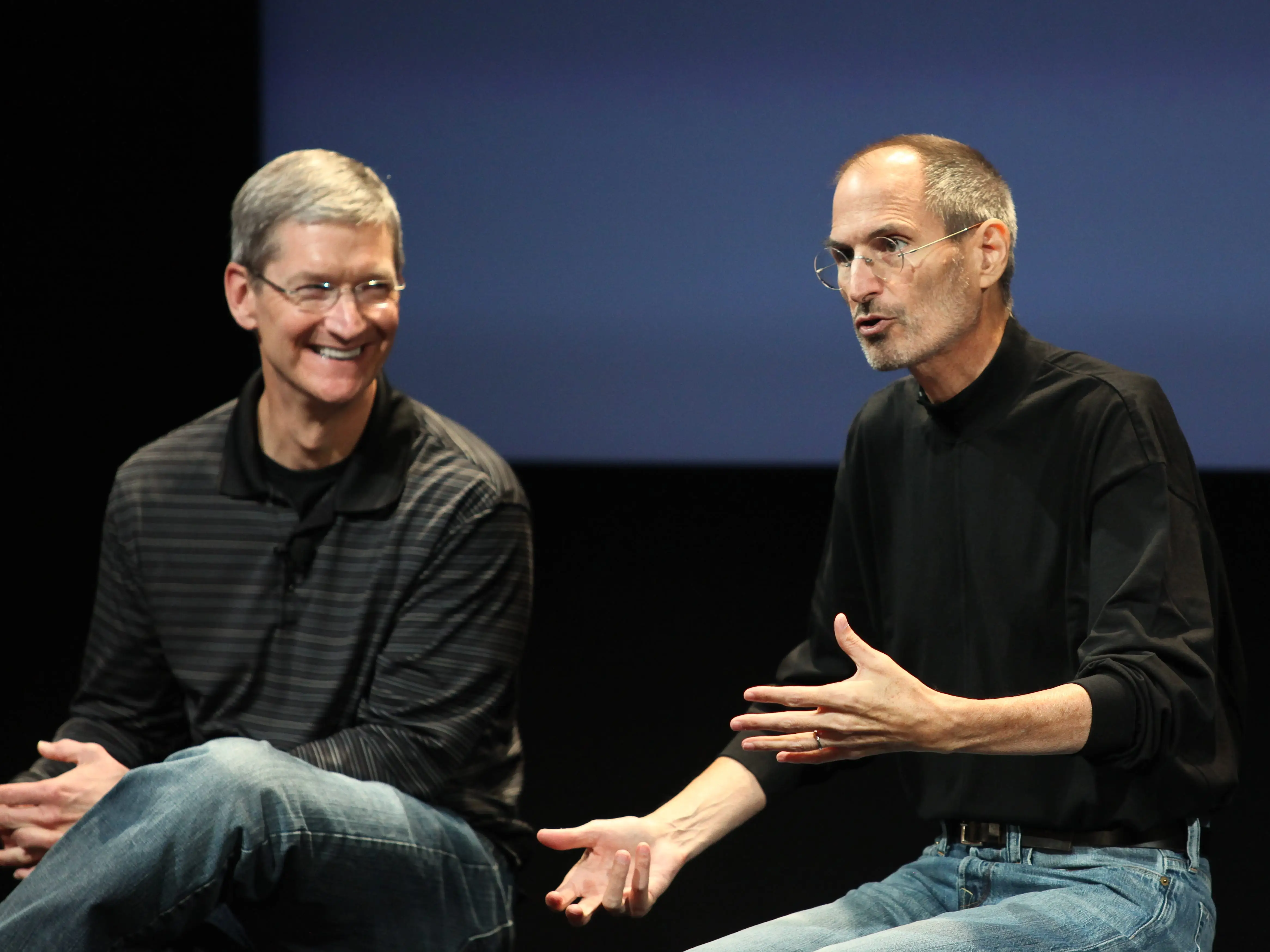 Tim Cook and Steve Jobs talking next to each other.