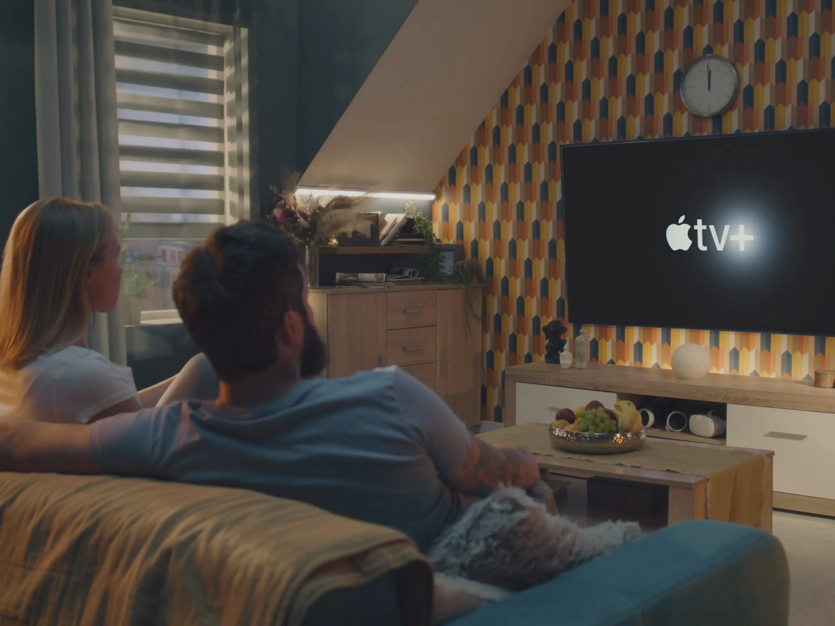 Two people watching a television with the Apple TV logo on the screen.