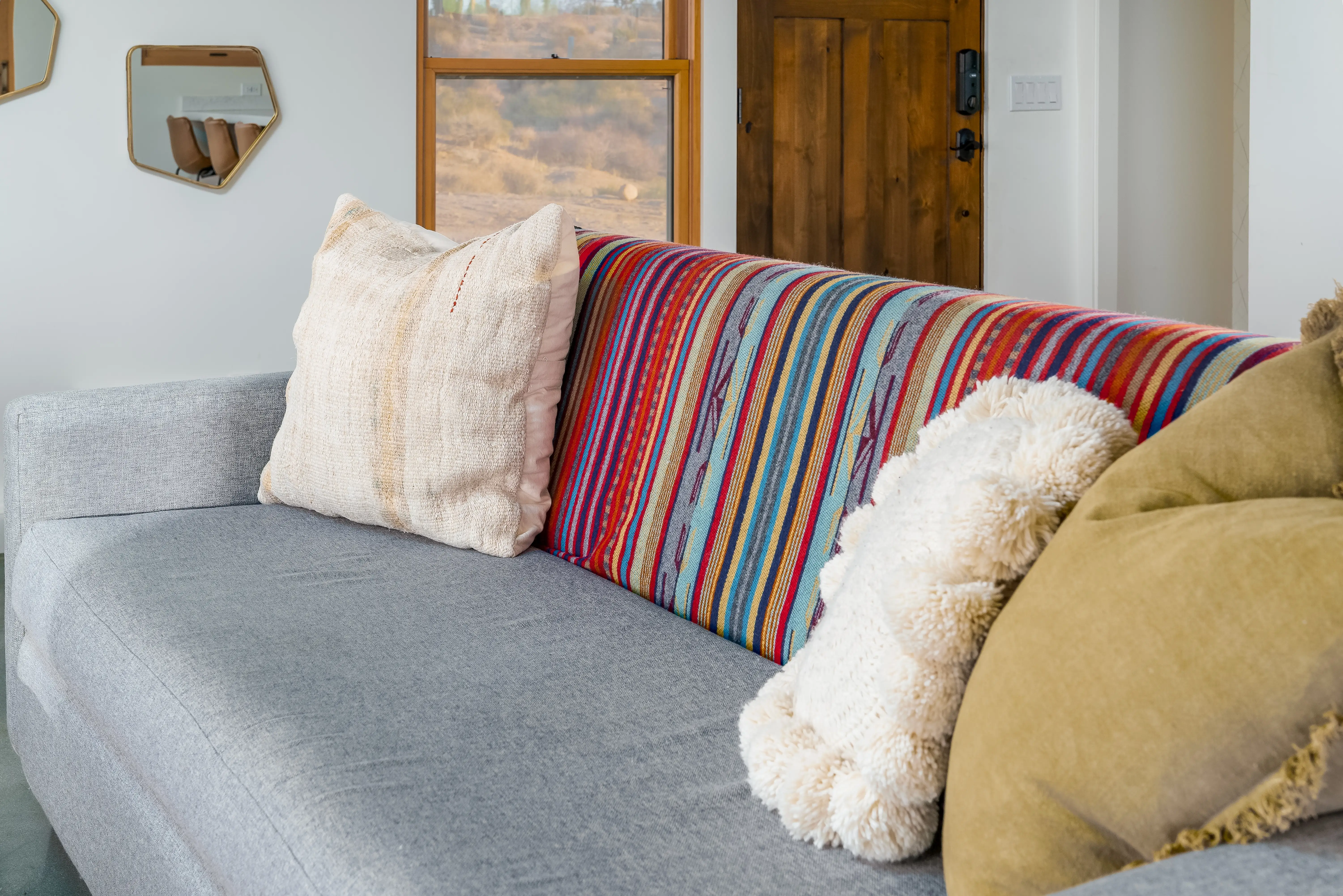 A gray couch with pillows and a colorful striped blanket.