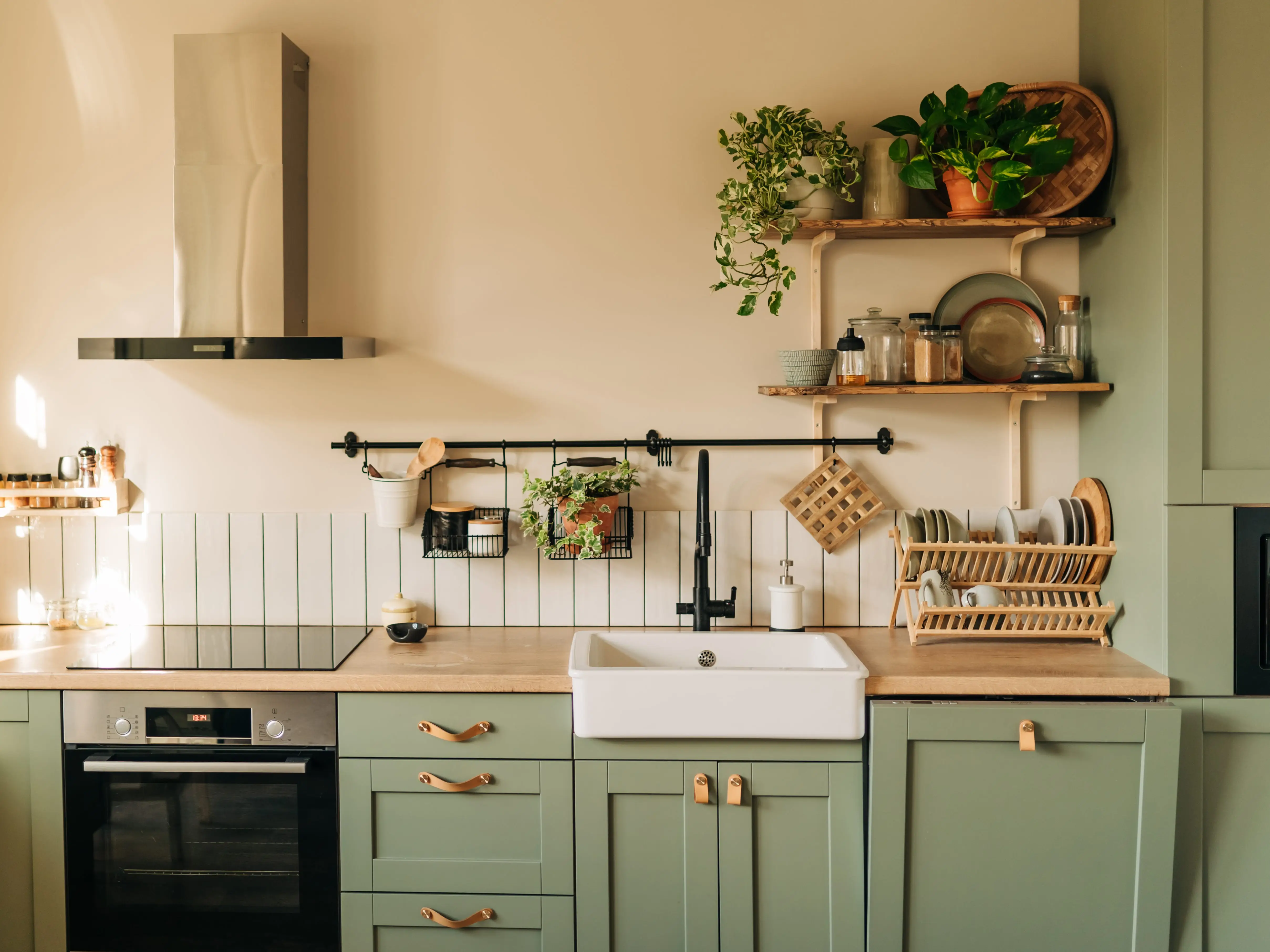 A kitchen with green cabinets and shelves filled with kitchenware and plants.