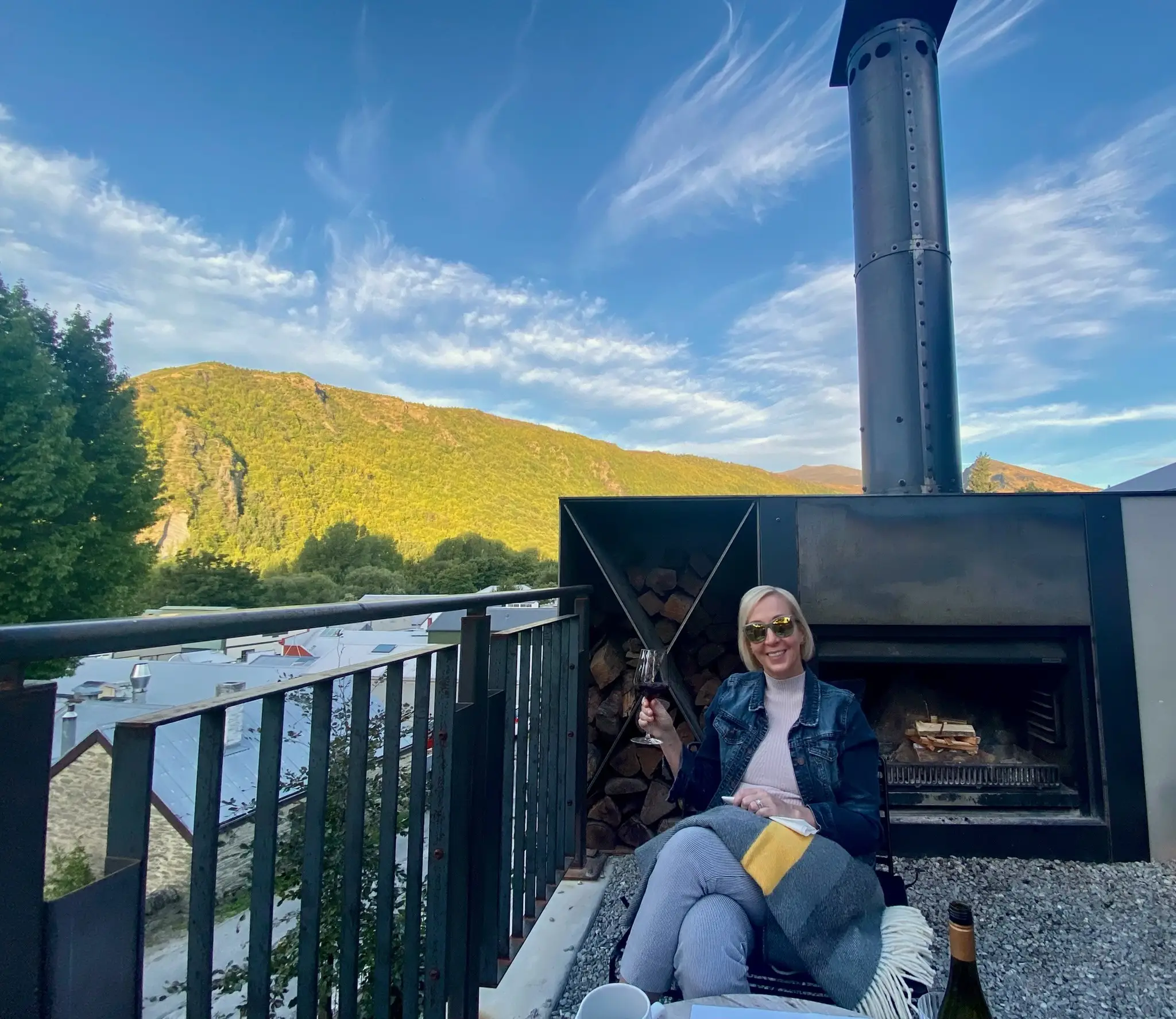 A woman holding a glass of wine in Arrowtown, New Zealand, during travels with her husband through the South Island.