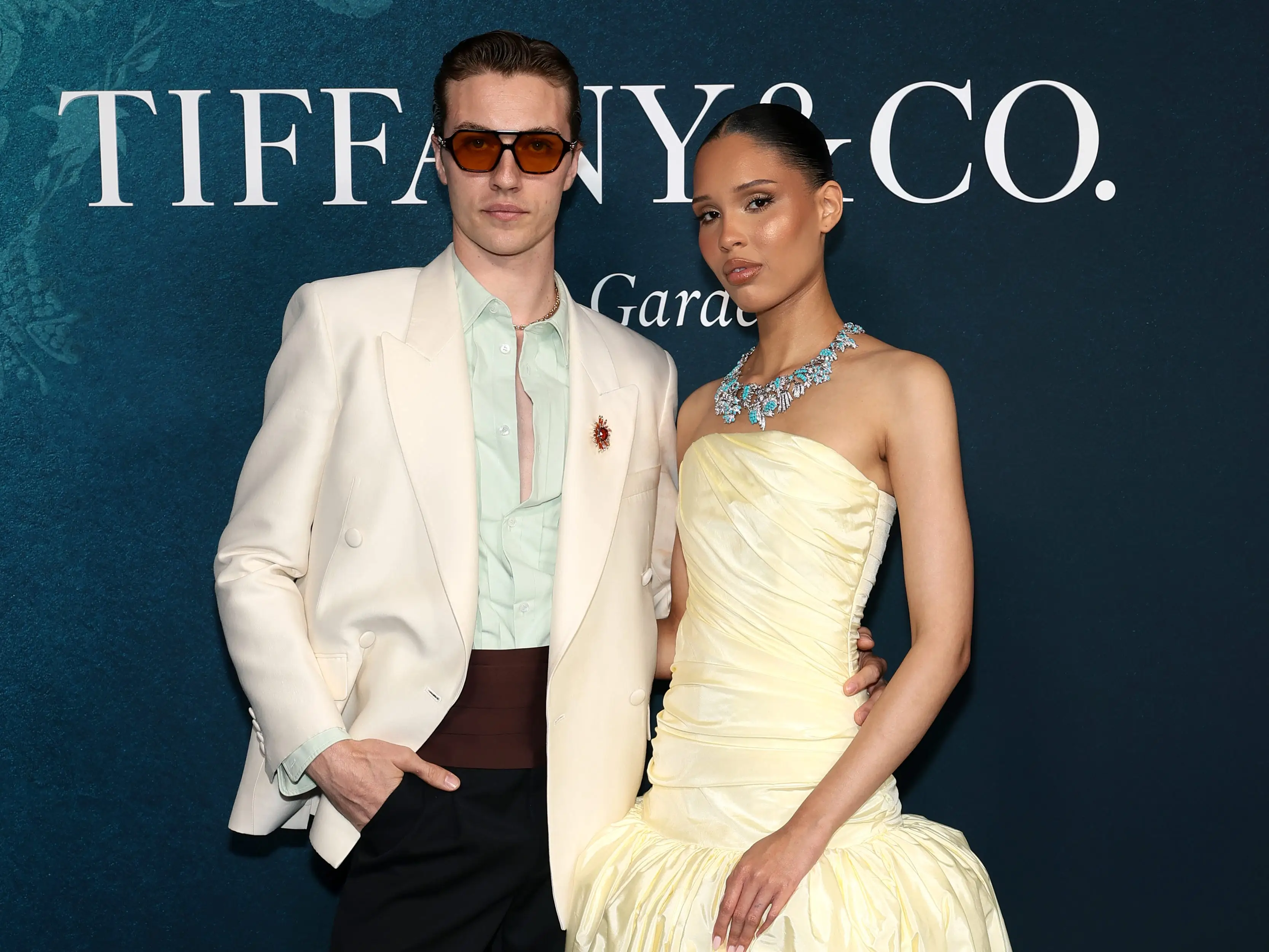 Nara Smith and Lucky Blue Smith pose in front of a step and repeat.