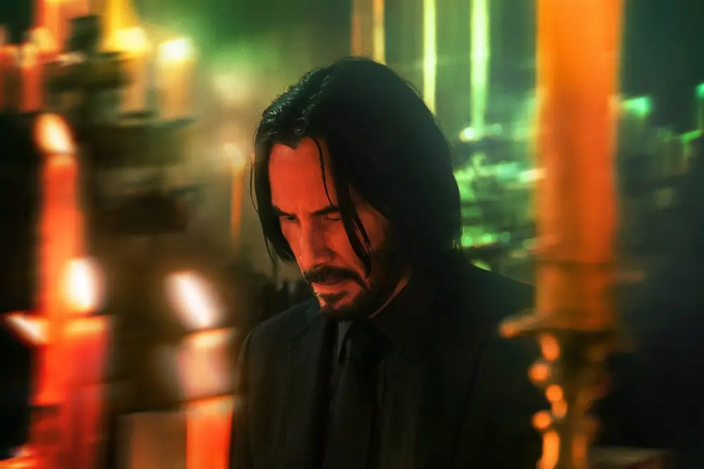 Keanu Reeves in a black suit around candles