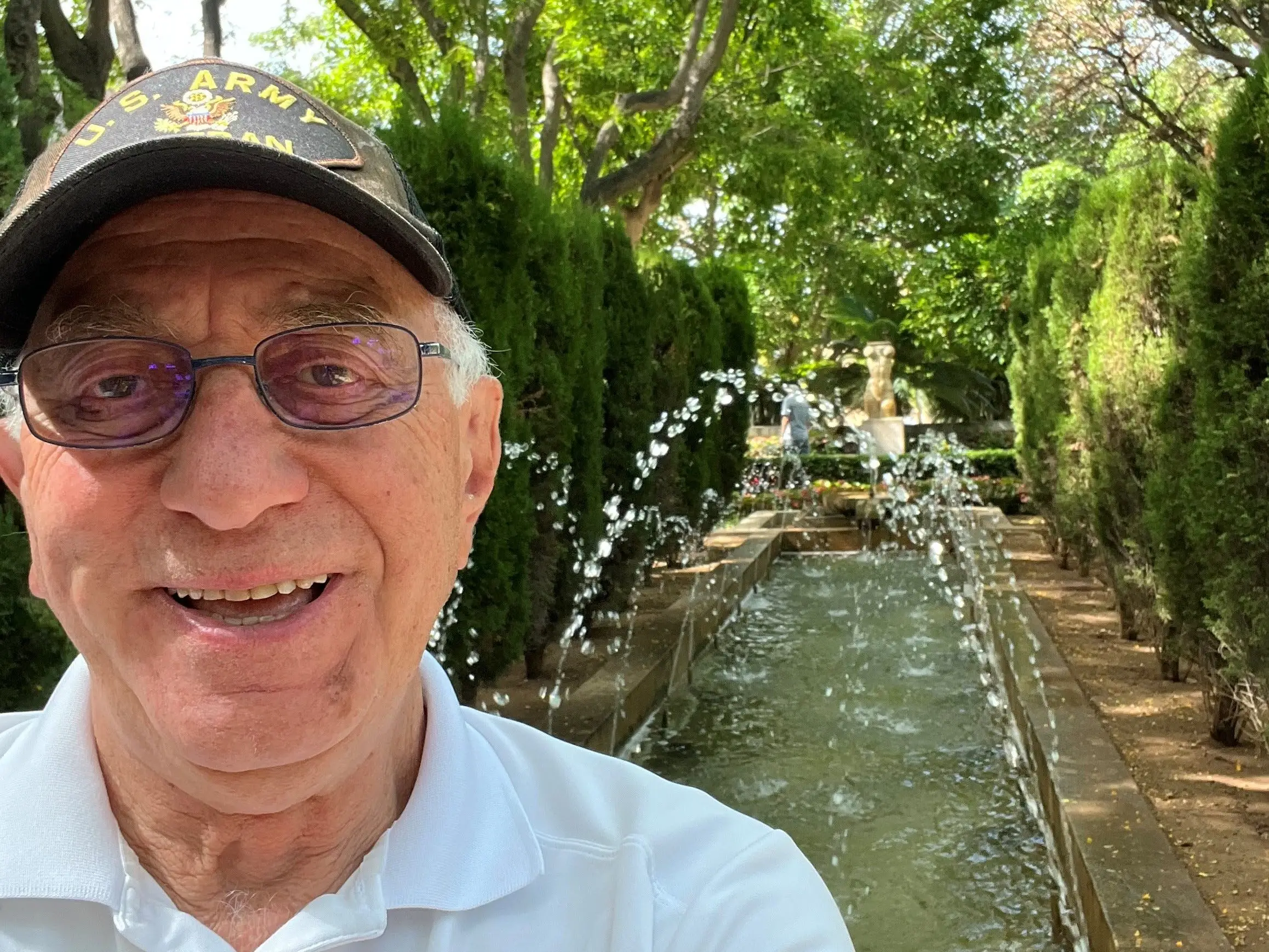 an older man takes a selfie in front of a fountain