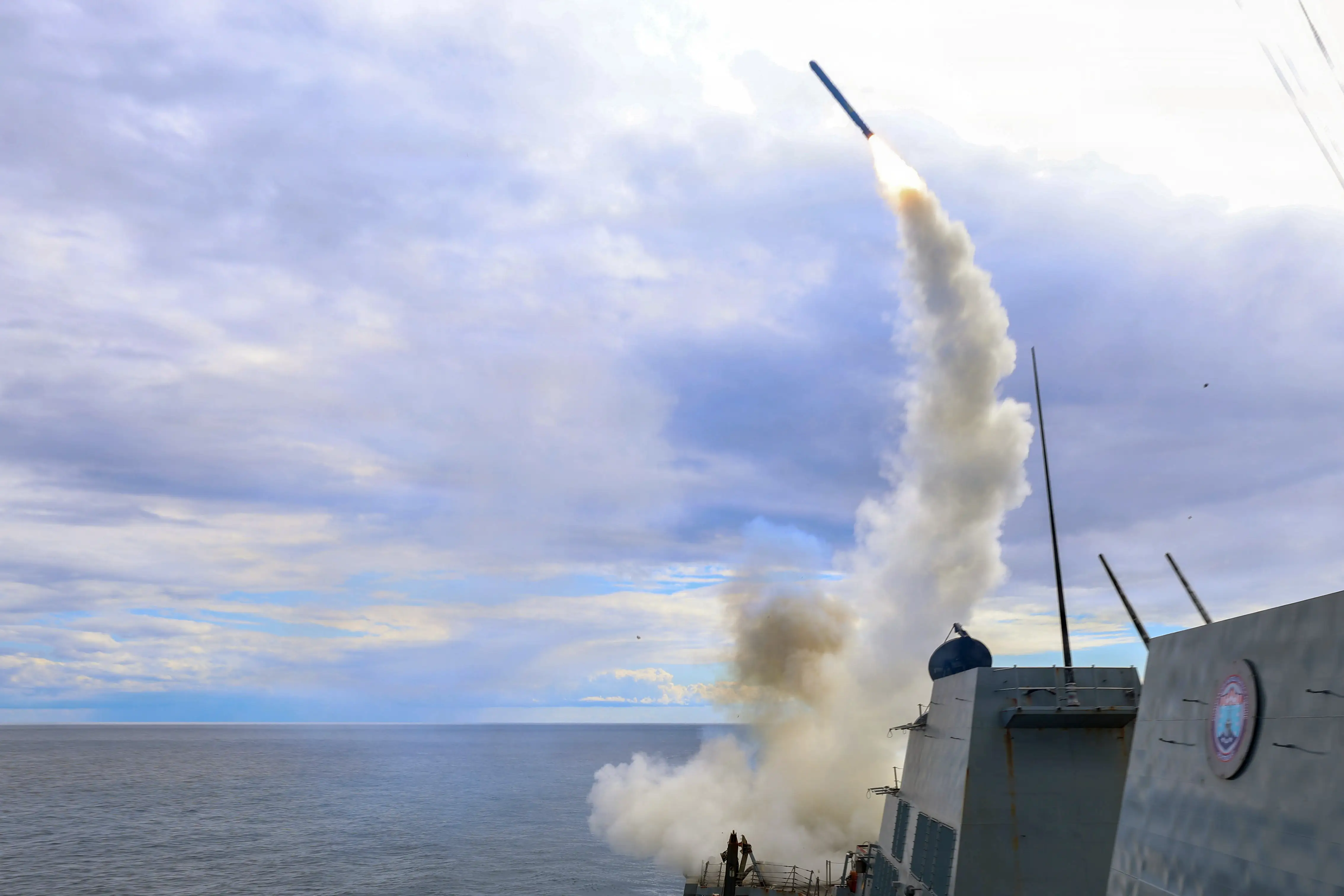 Smoke as a is missile launched from a ship under a cloudy and blue sky