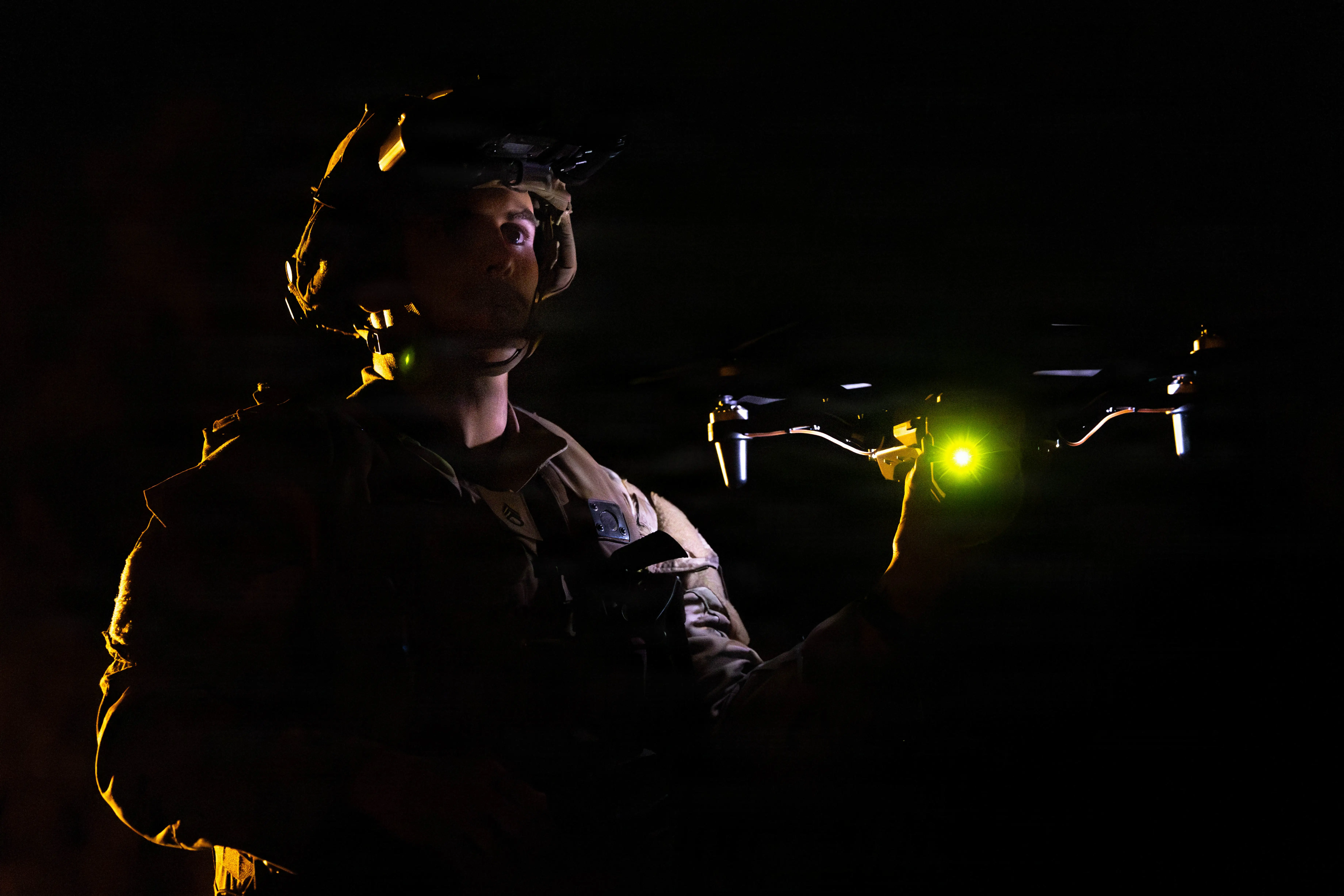 A soldier holds a drone at night in the dark.