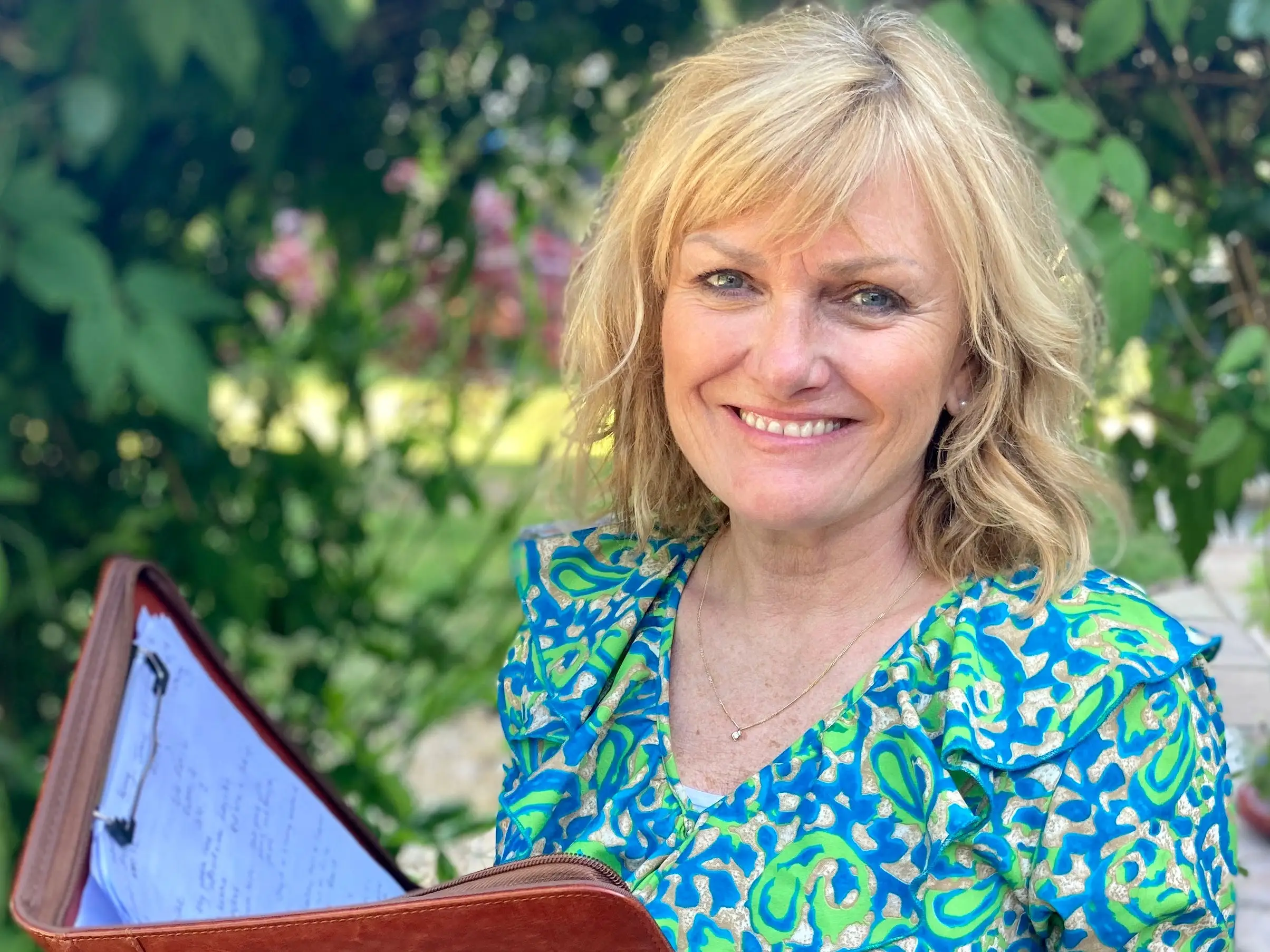 A woman in a green-and-blue patterned dress holding a brown folder.