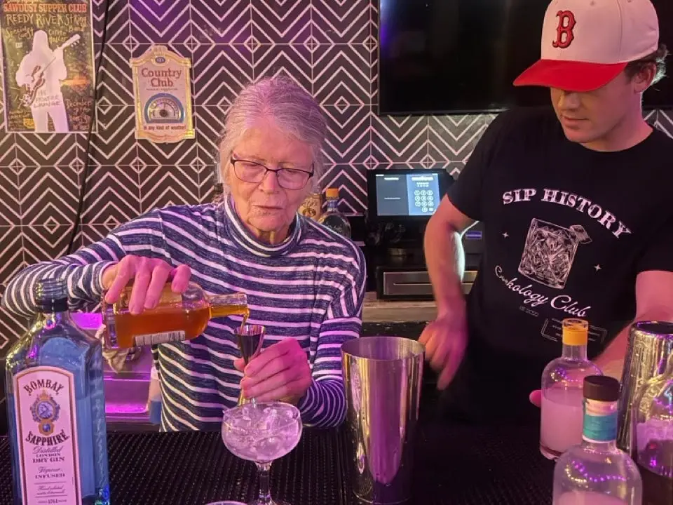 Woman pouring cocktail with man in hat standing next to her