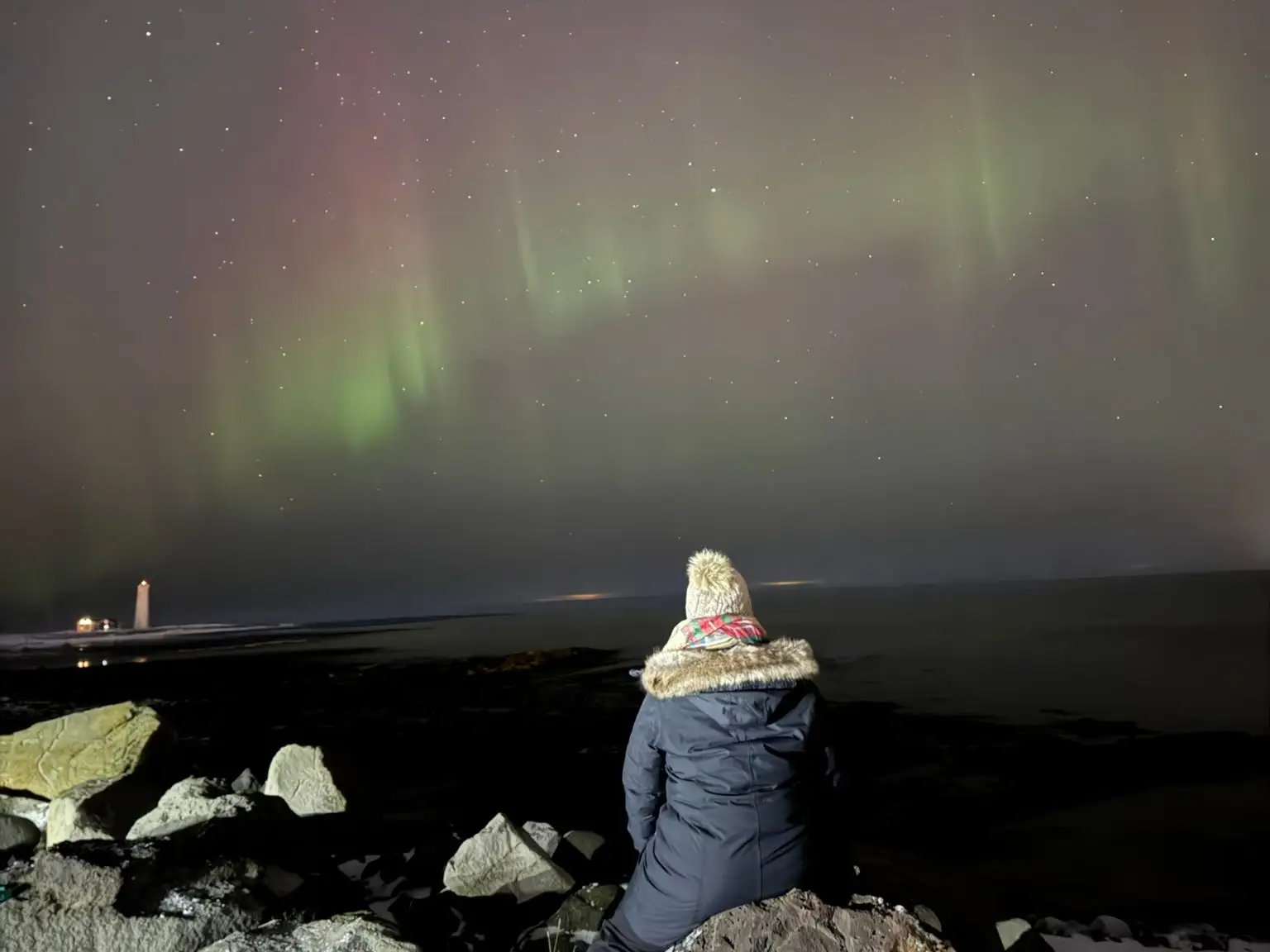 Taylor sits on a rock, looking up at the northern lights.