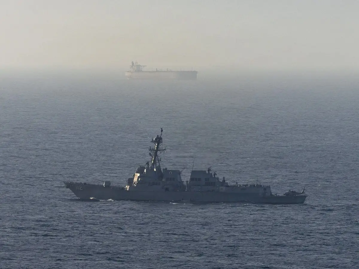 A US Navy destroyer operates near a merchant vessel in the Middle East.