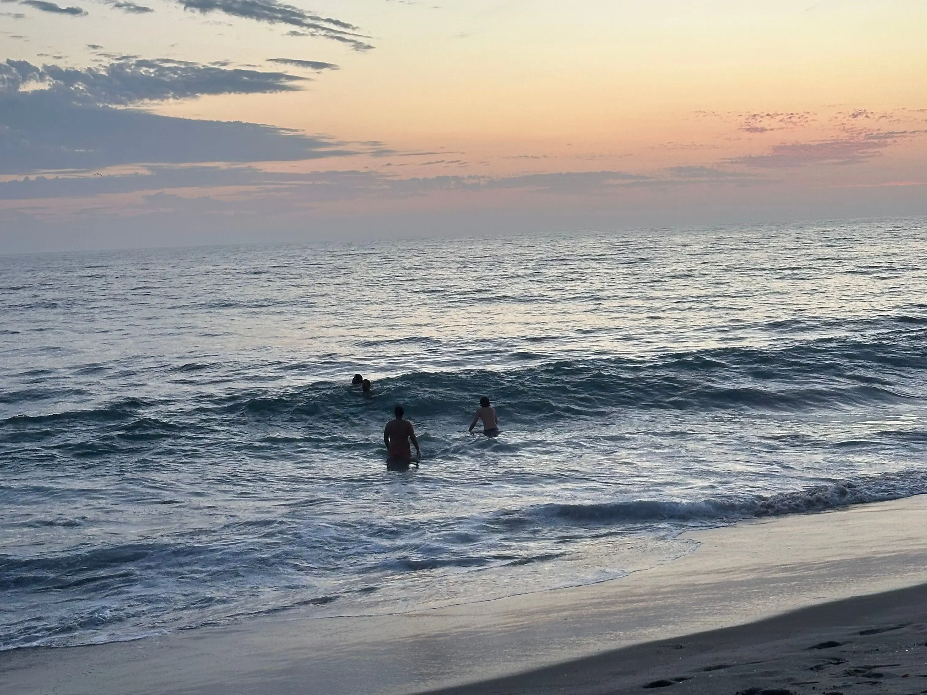 4 men swimming in the ocean, the sun is setting behind them.