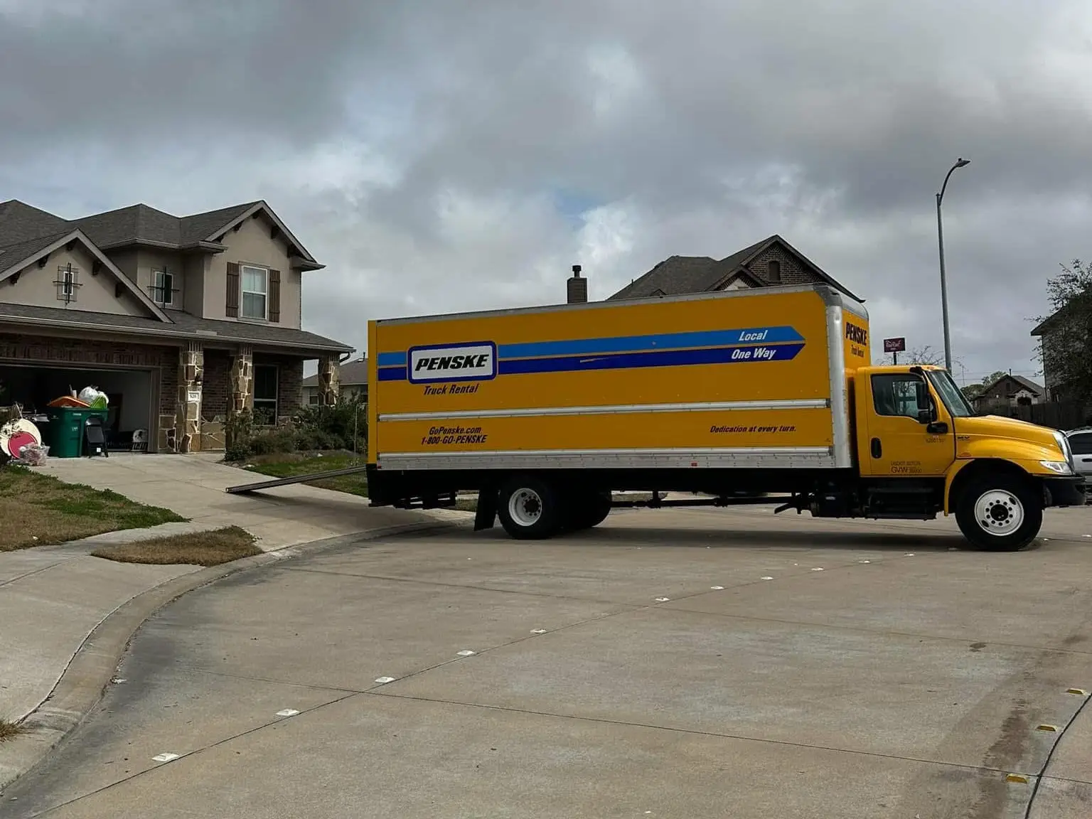 A Penske moving truck parked in front of a large two story home.