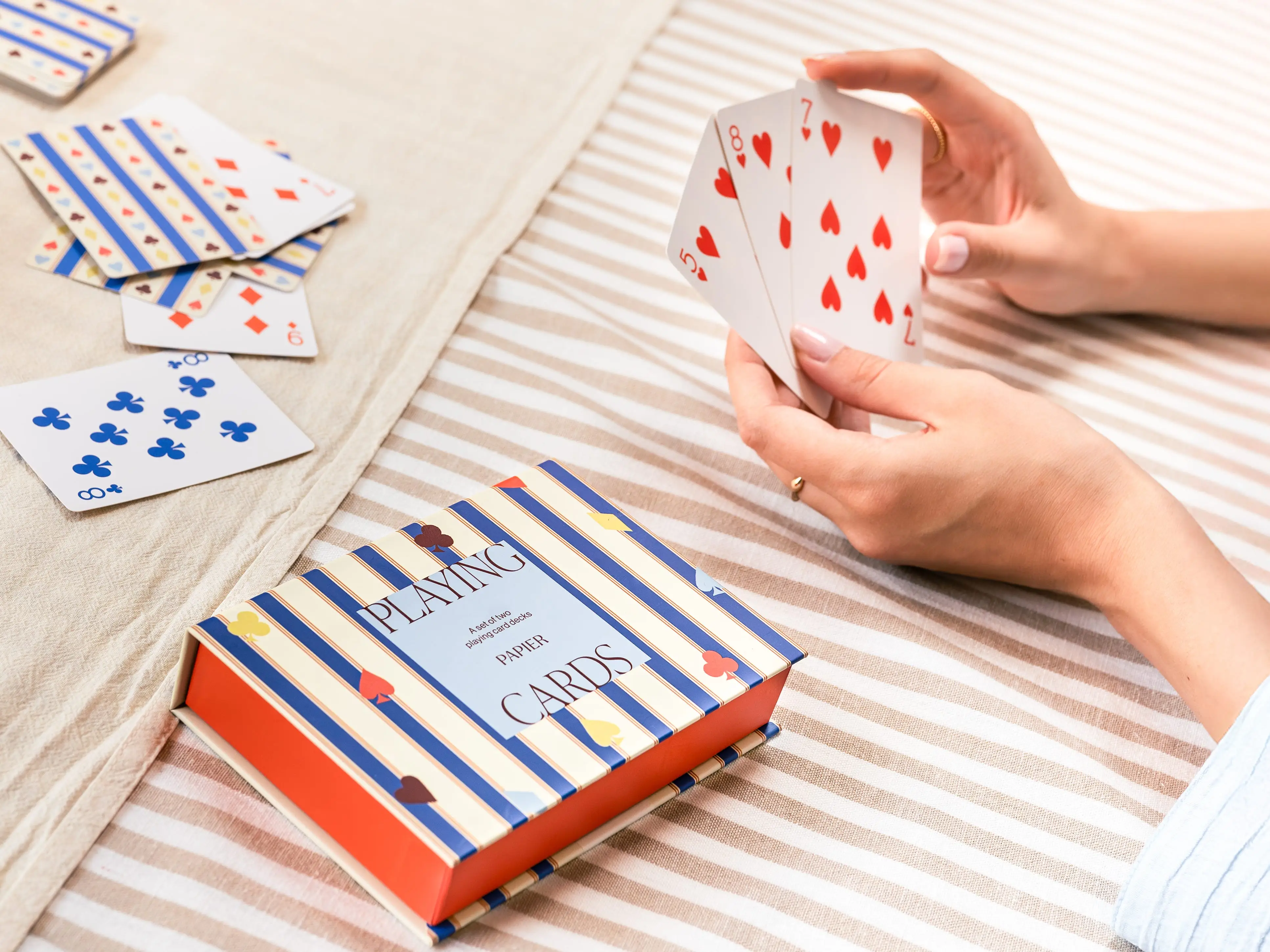 Papier's 'Stripes & Suits' playing cards set on a table with a person pictured holding some of the cards.