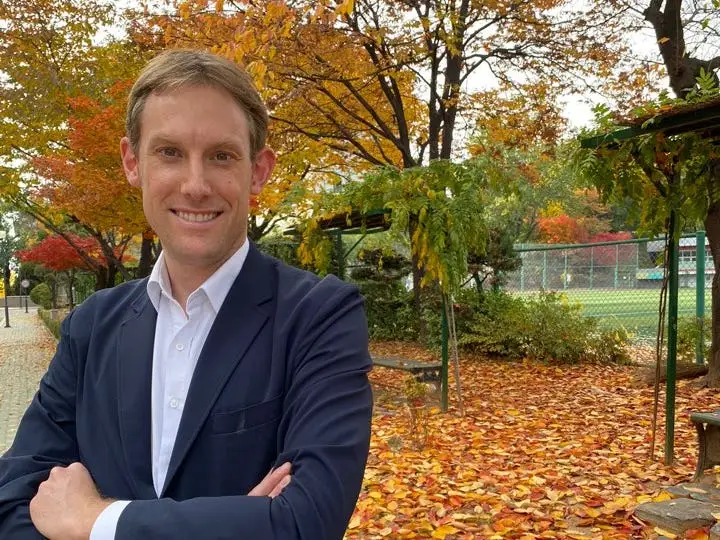 Derek Laan wearing a balzer and posing with autumn trees in the background.
