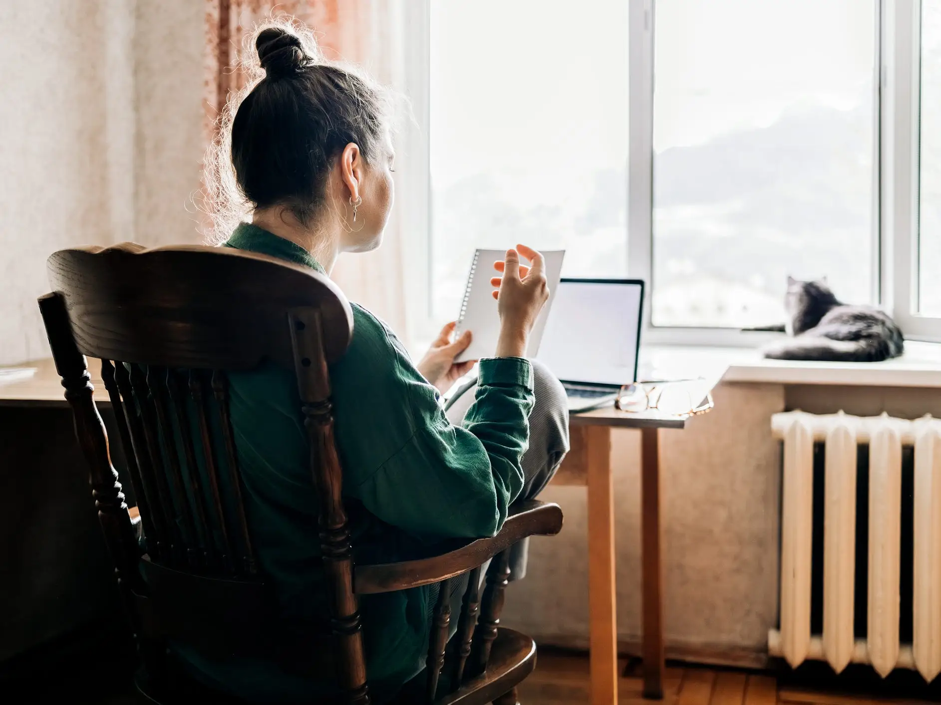 A woman working from home and looking at her laptop and notebook.