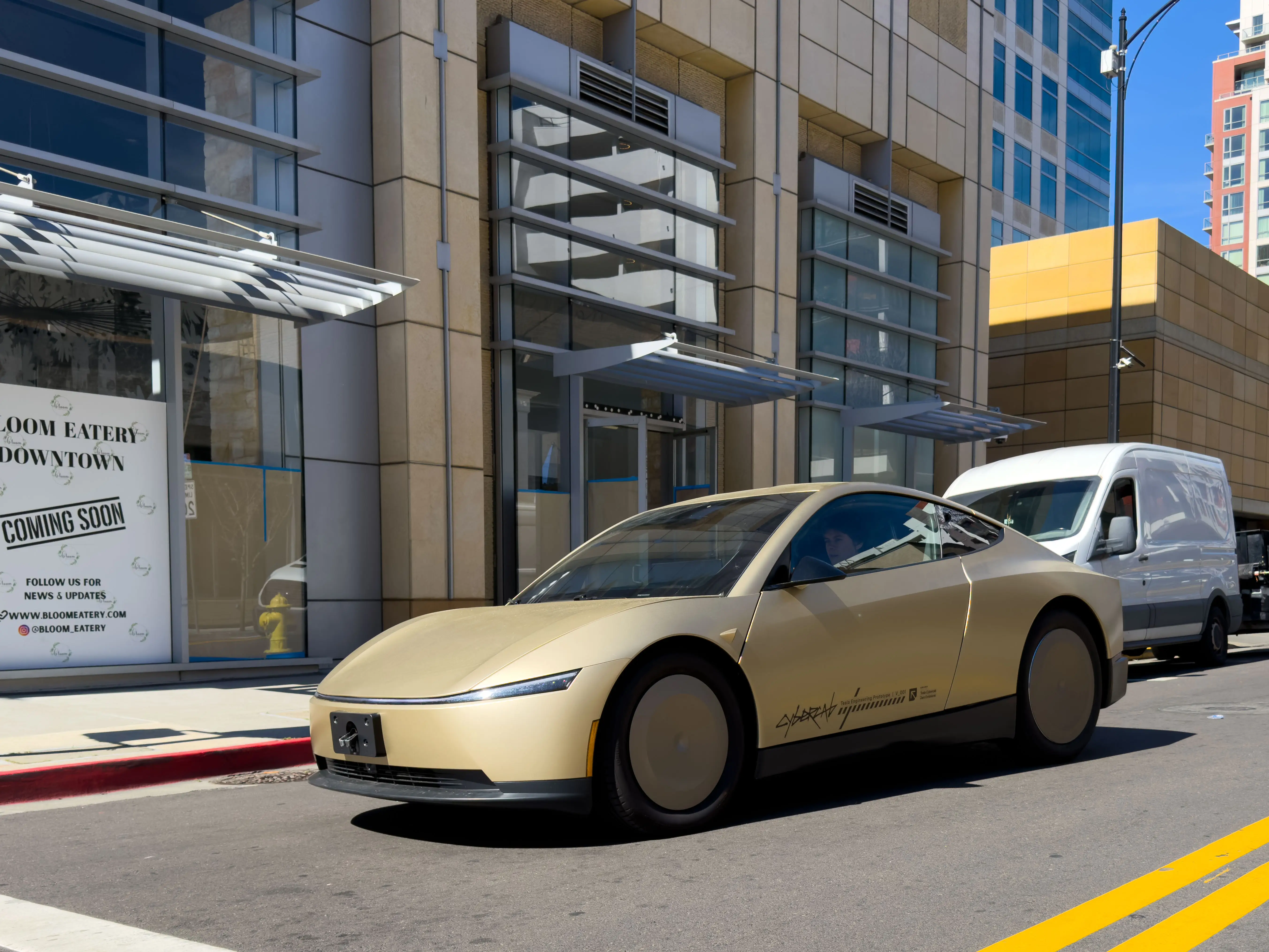 A gold Tesla Cybercab drives down a city street.