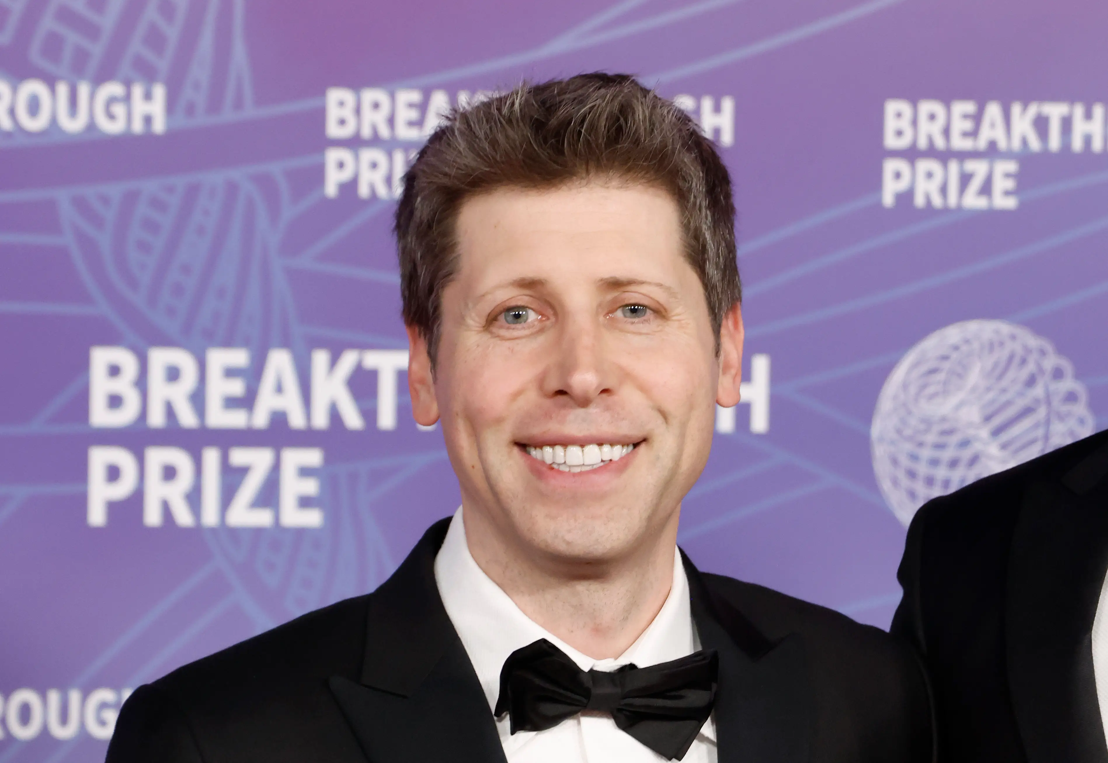 Sam Altman, smiling and wearing a bowtie, gets his picture taken on a red carpet.