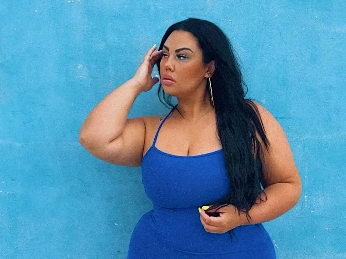 A woman in a blue dresses poses against a blue backdrop.