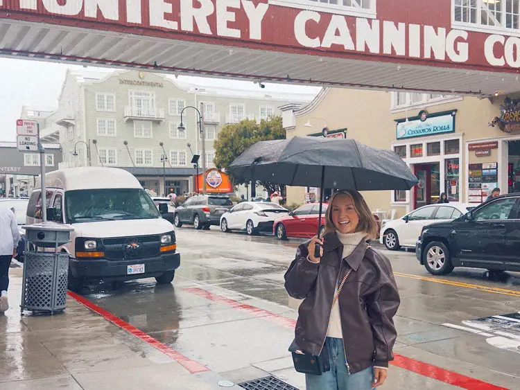 Chloe stands on the street in Monterey, California, with an umbrella.