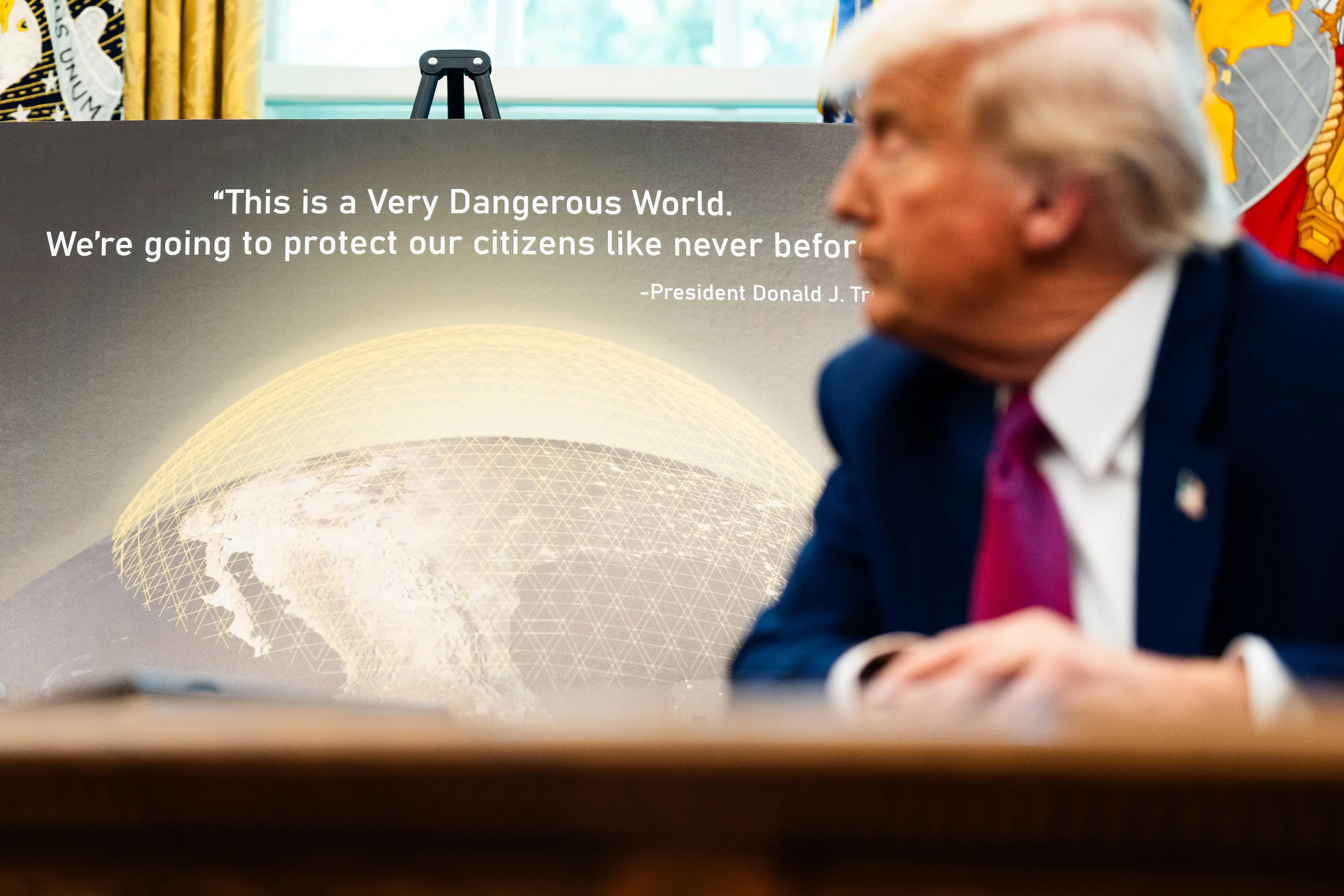 US President Donald Trump sits in front of a poster showing Golden Dome.