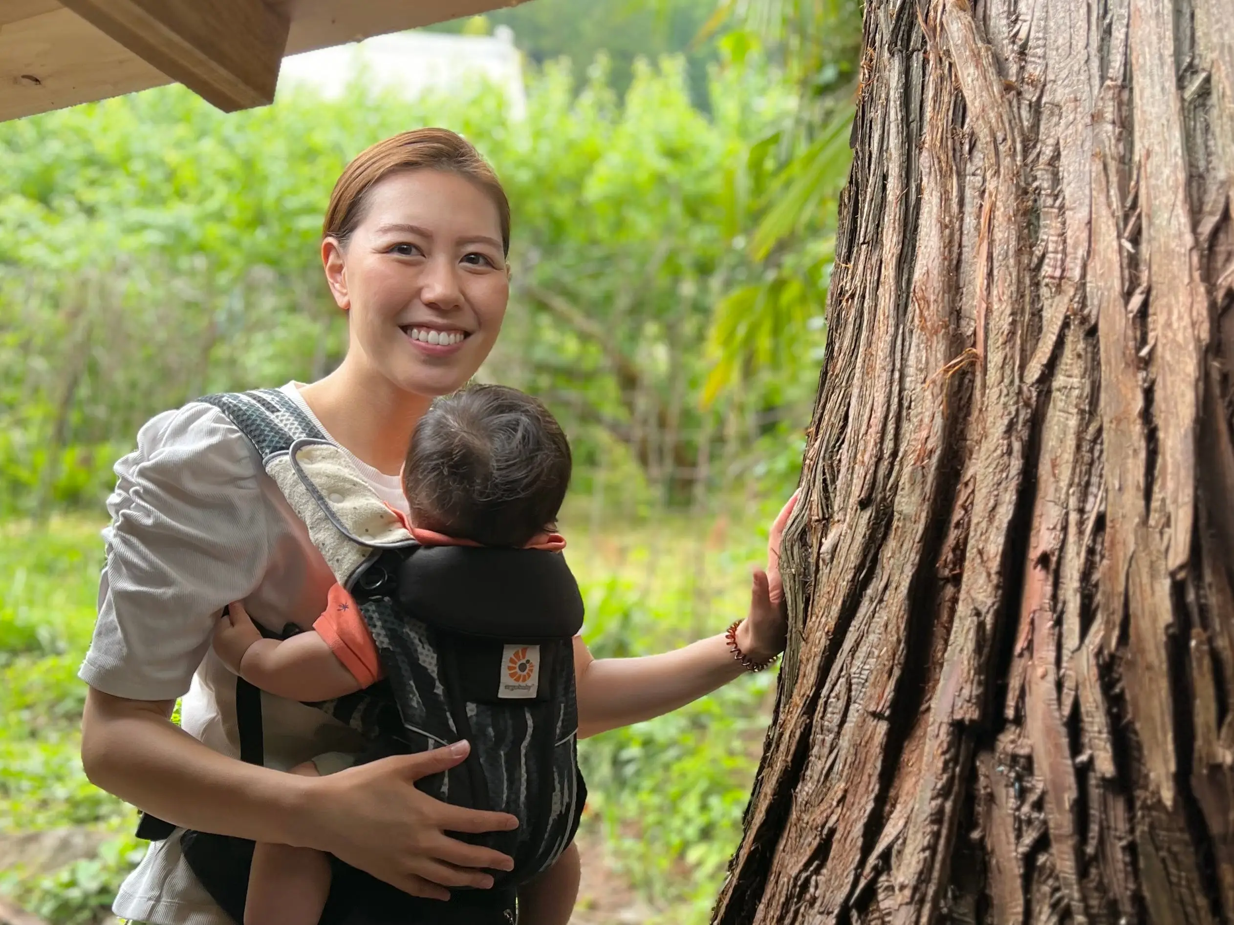 A woman holding her baby and leaning on a tree in Japan.
