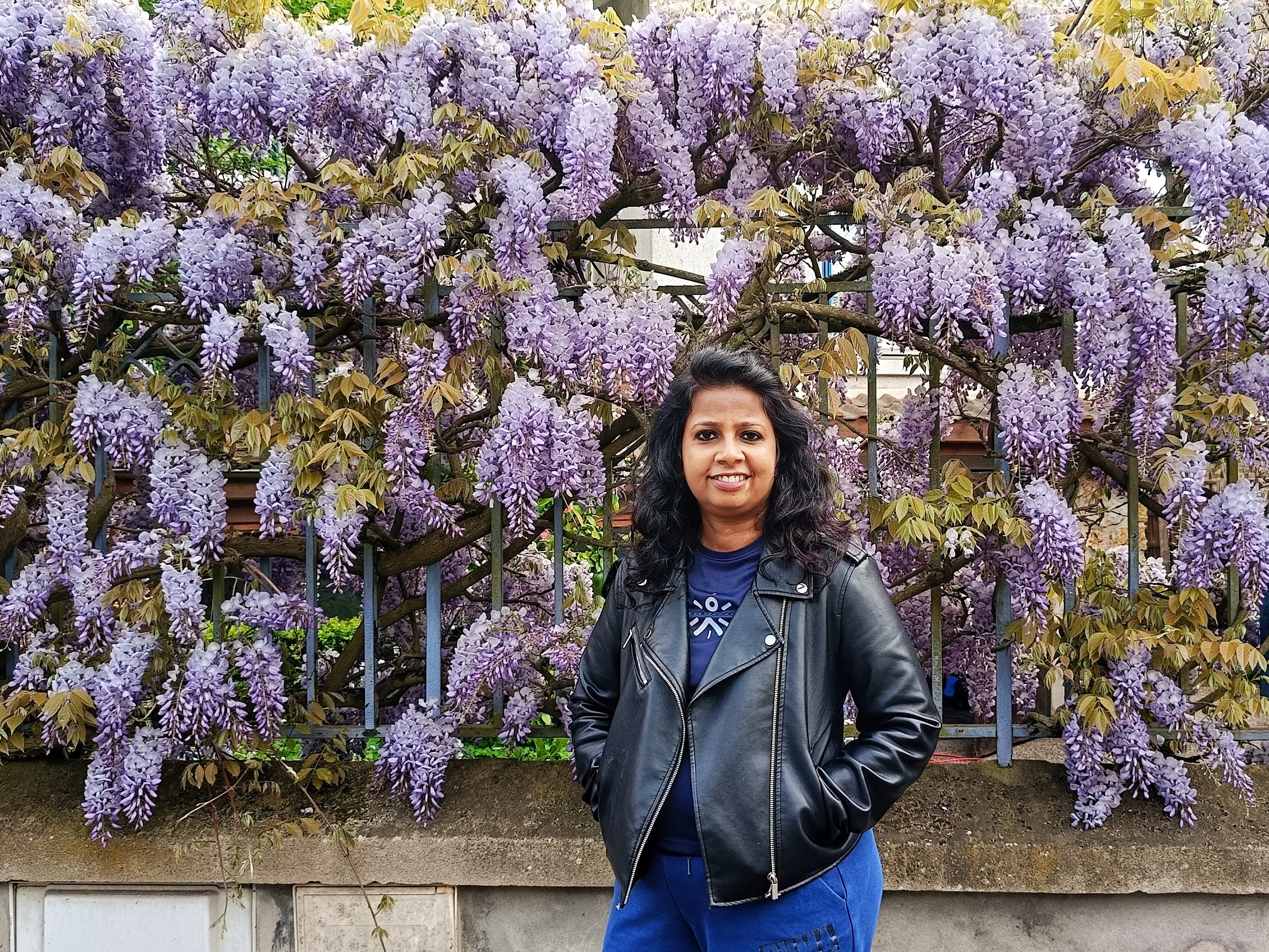 Rathina Sankari poses in front of a fence covered in purple flower.