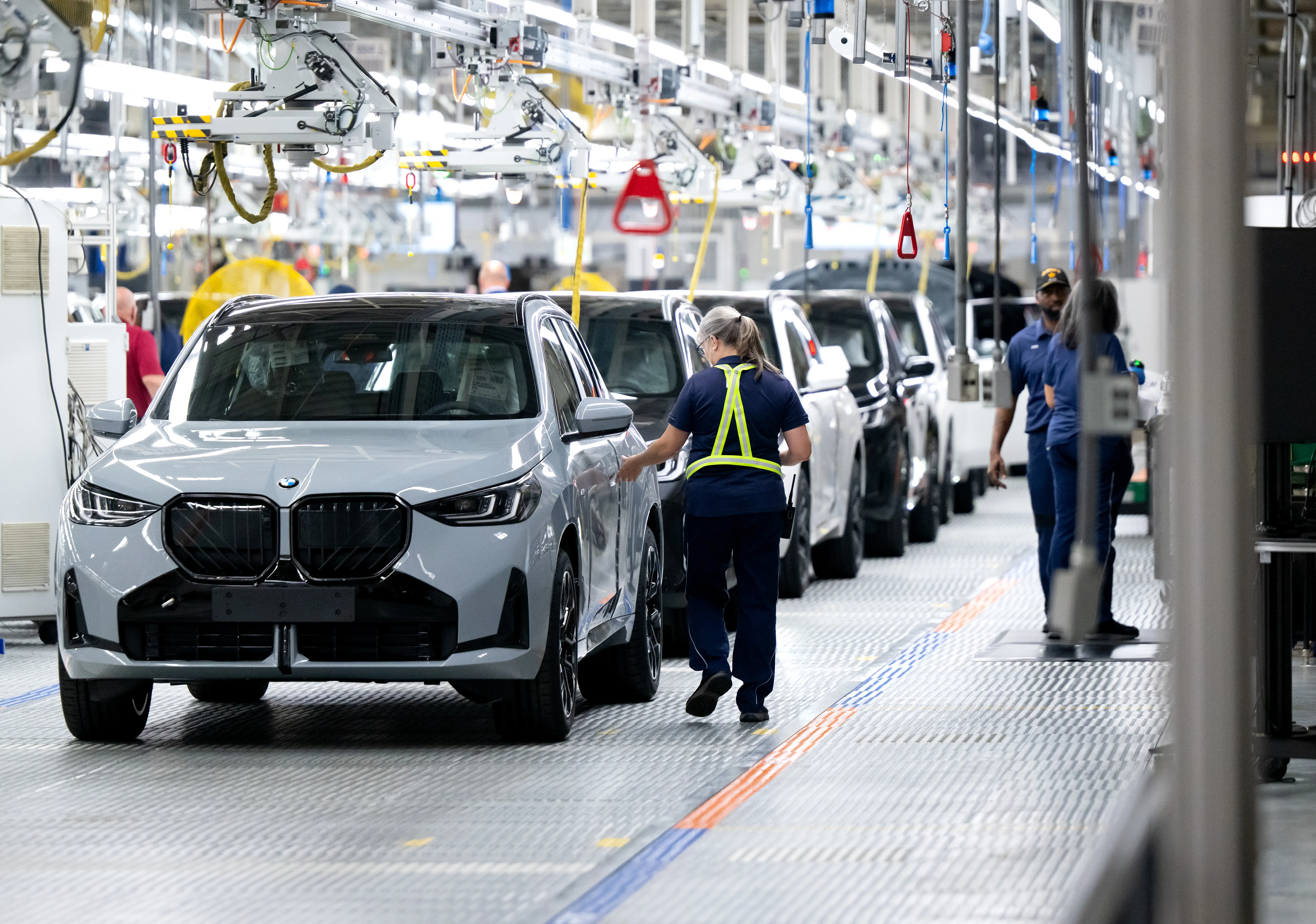 Workers stand on a production line at a BMW plant in South Carolina as SUVs stand on the factory floor.