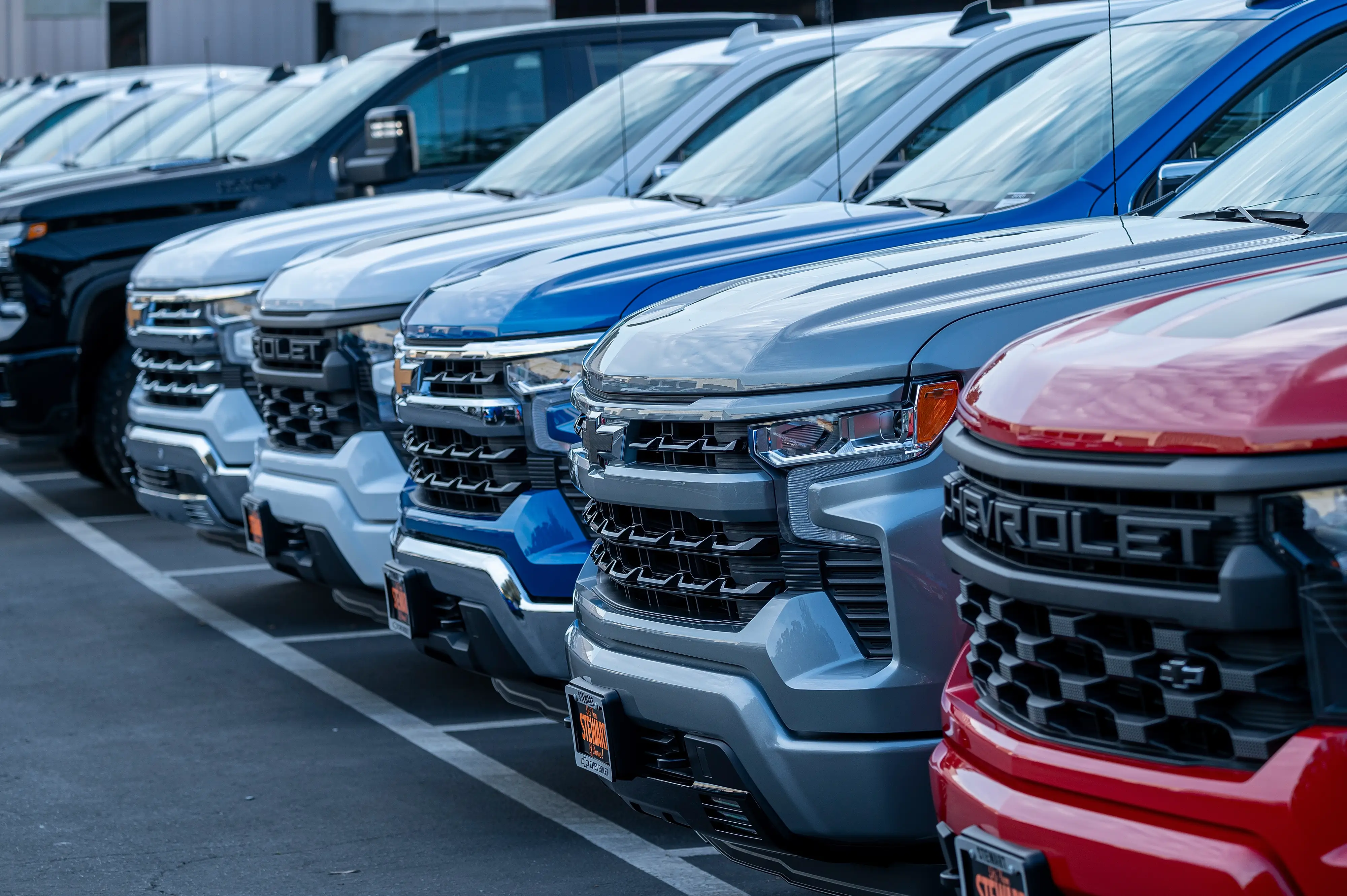 A line of full-size Chevy vehicles are parked on a dealership lot.