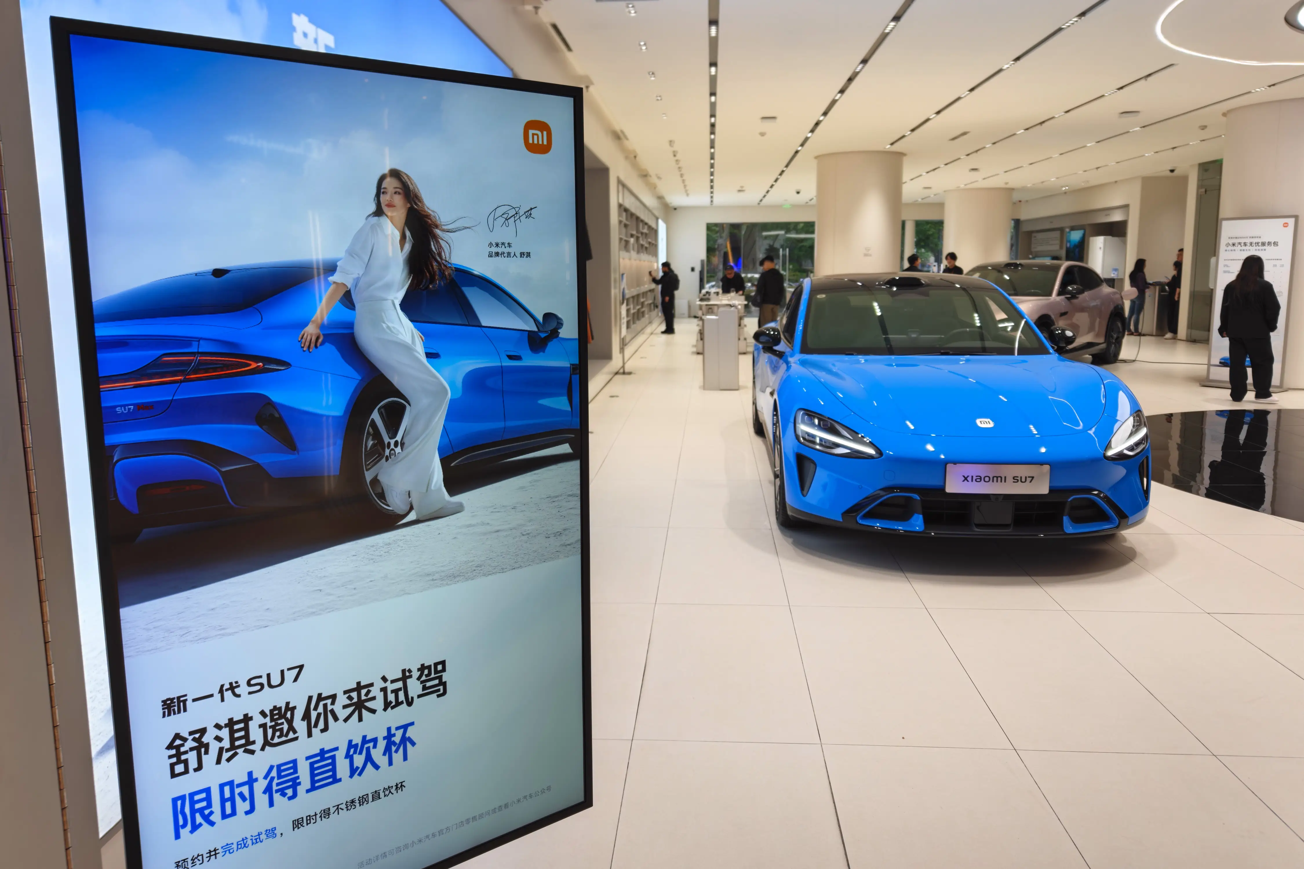 A blue Xiaomi SU7 is parked in a Chinese dealership showroom.