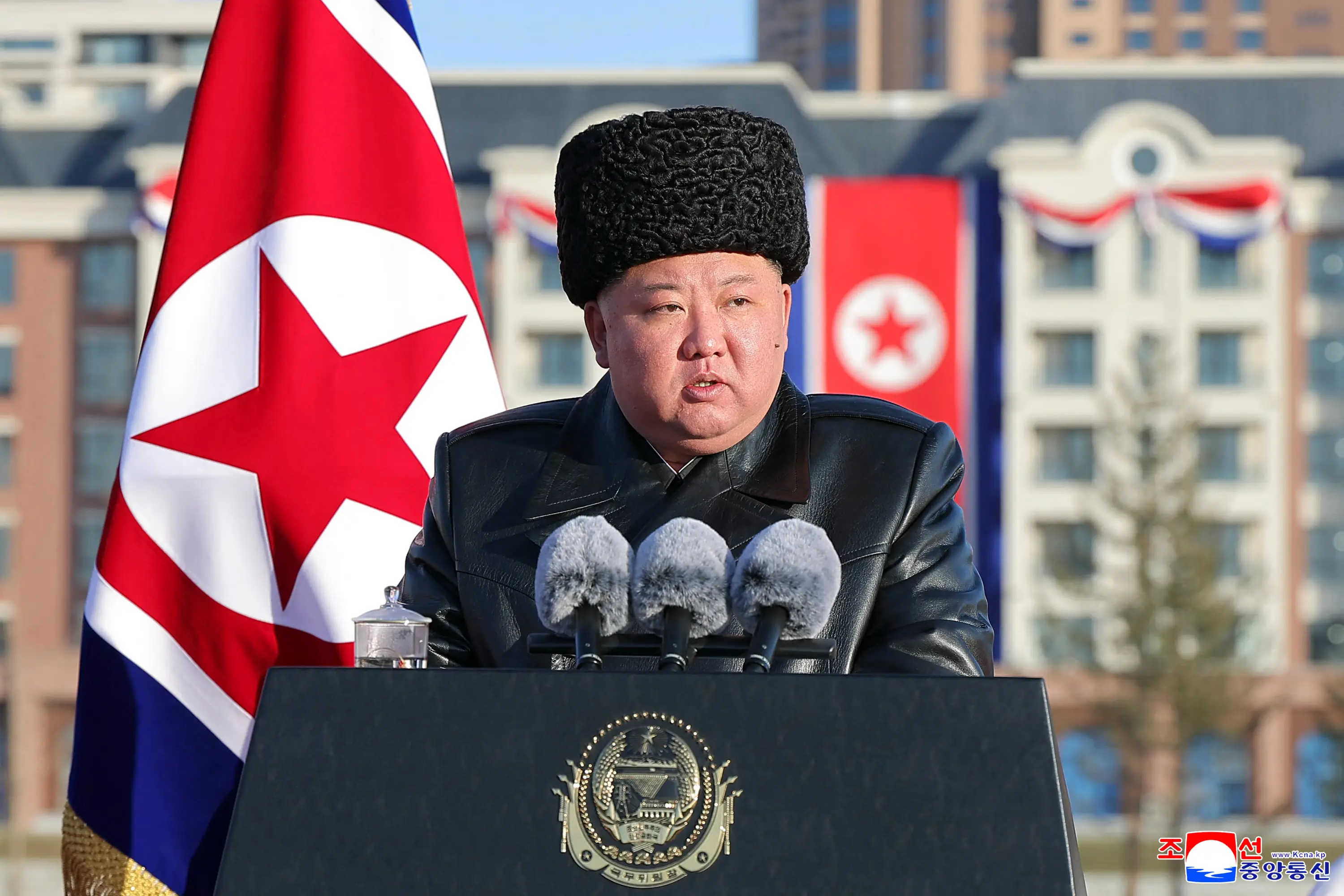 Kim, wearing a hat, speaks in front of a rostrum.