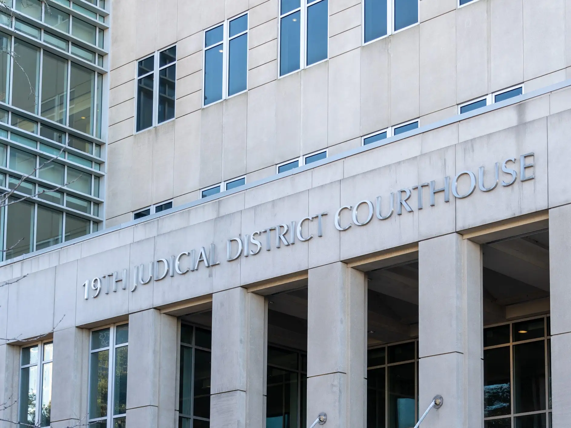 The entrance of the 19th Judicial District Courthouse is shown on a tall concrete building with large windows.