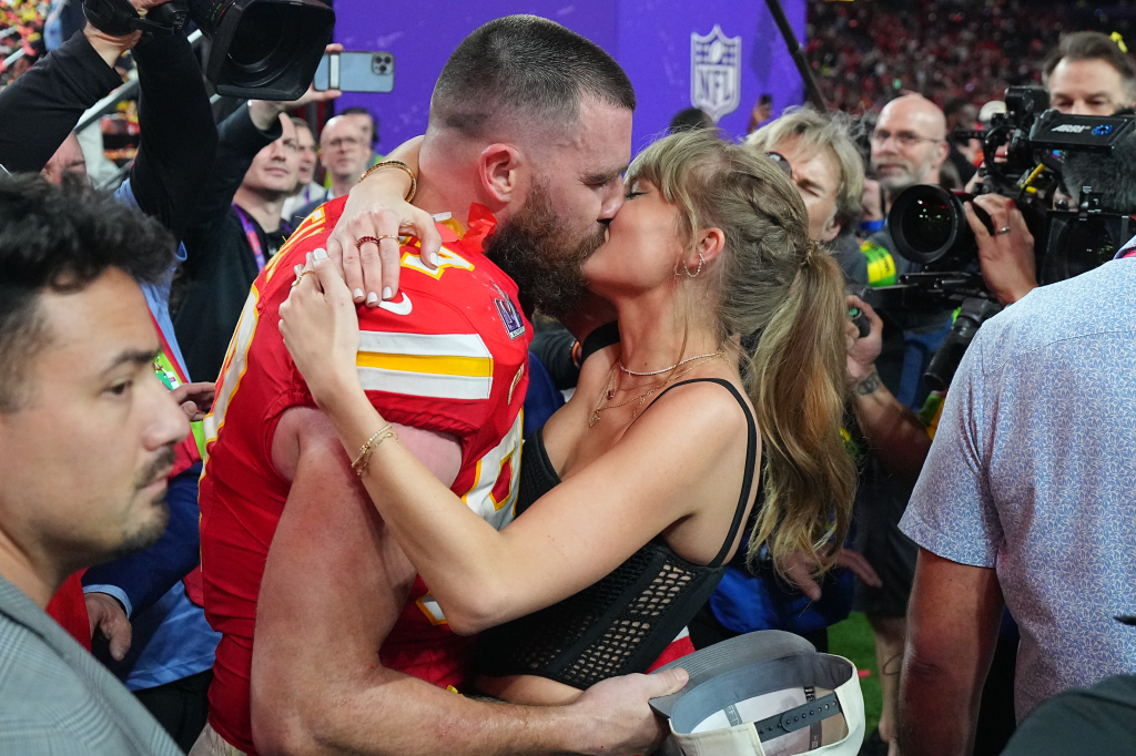 Travis Kelce in a red Kansas City Chiefs jersey kissing Taylor Swift, who is wearing a black top.