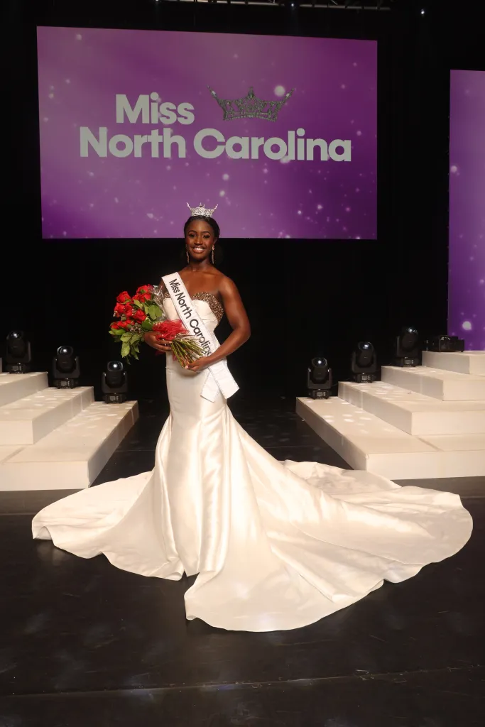 Miss North Carolina holding a bouquet of red roses and wearing a white gown and a crown.
