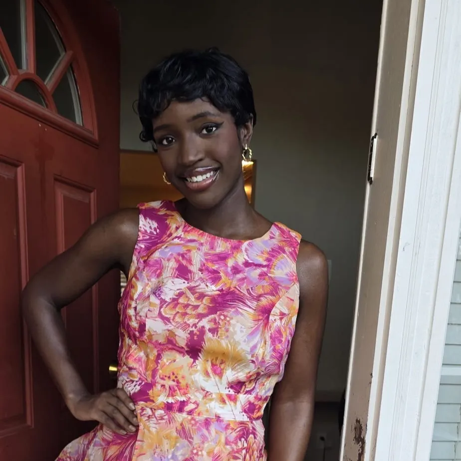 A woman in a floral dress smiling in a doorway.