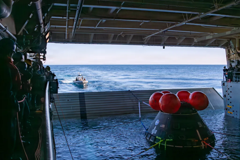 NASA Orion test article in the water next to a ship with a small boat approaching.
