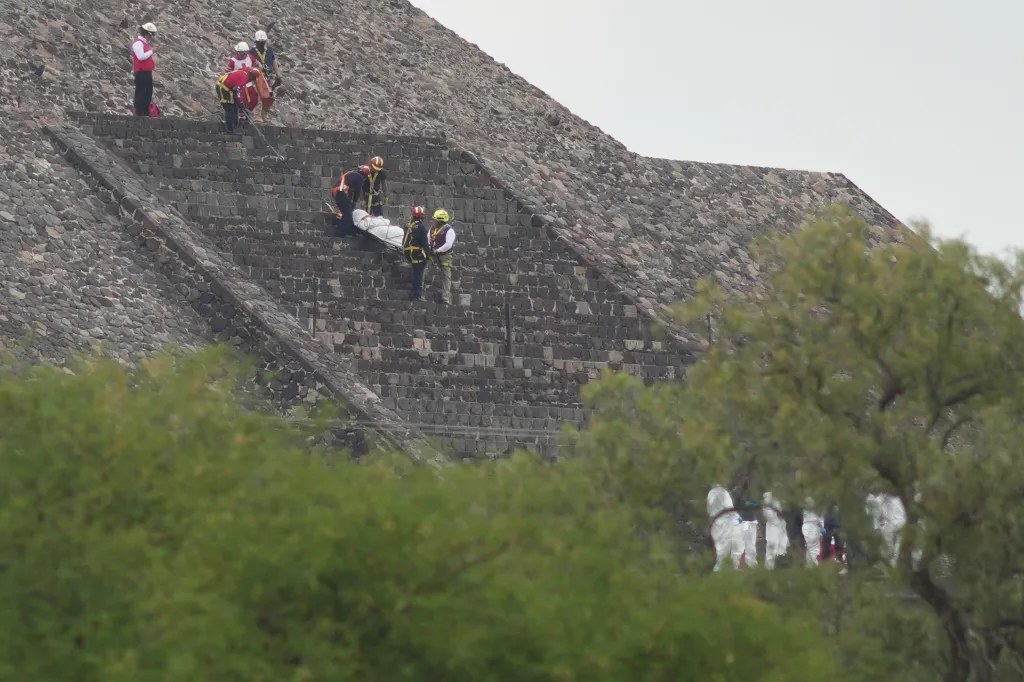 Emergency responders carrying a person on a stretcher down the steps of a stone pyramid.