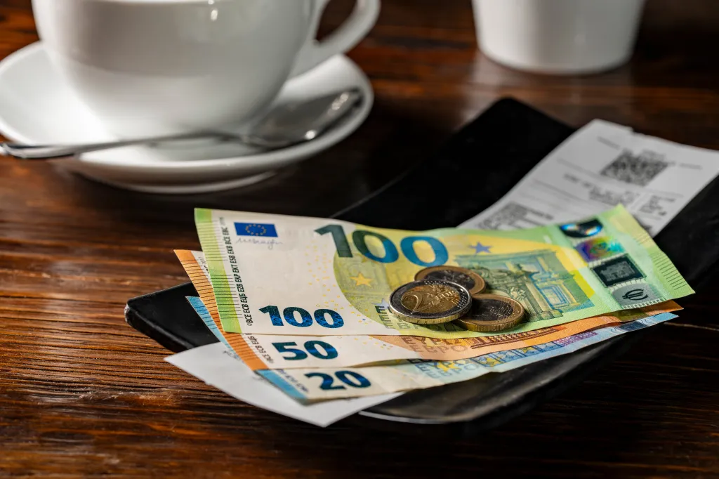 Euro banknotes and coins in a tip tray with a restaurant bill.