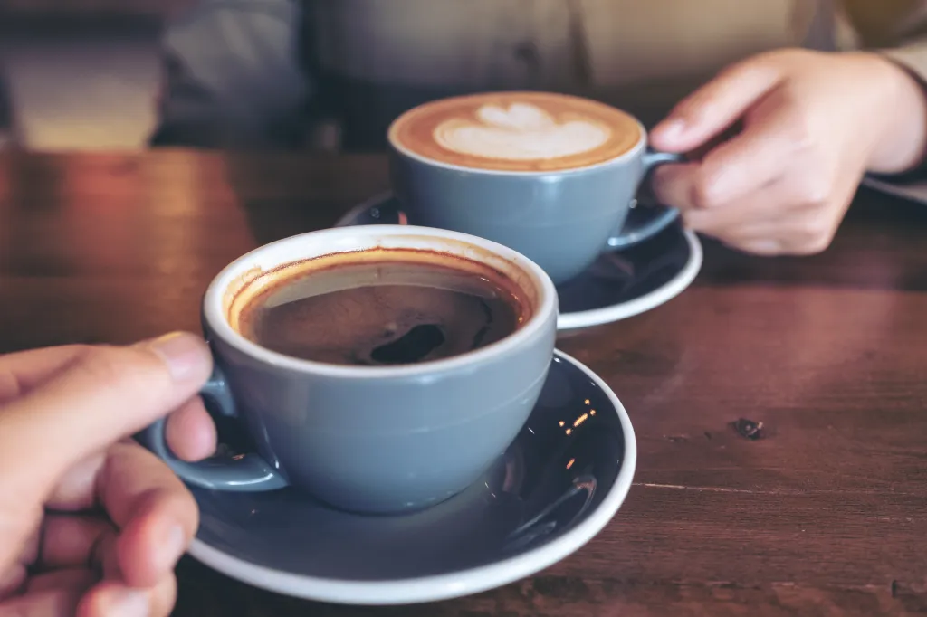 A close-up of a man and a woman clinking blue coffee mugs on a wooden table.