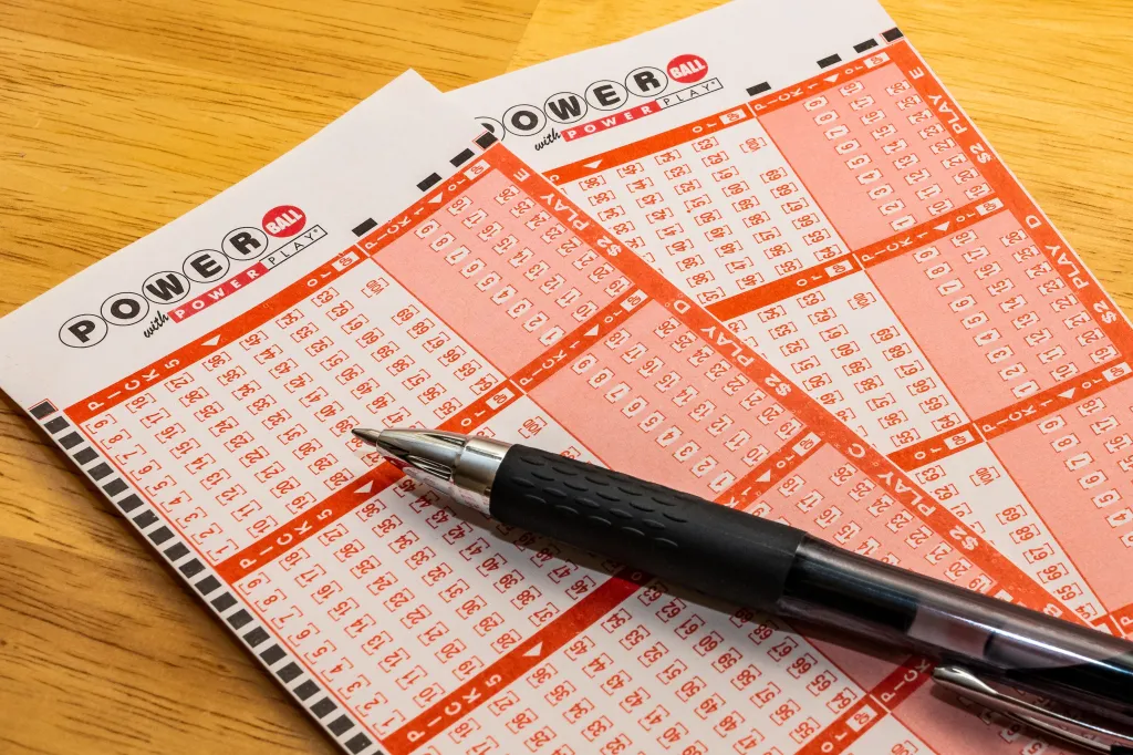 Powerball lottery tickets with a pen on a wooden surface.
