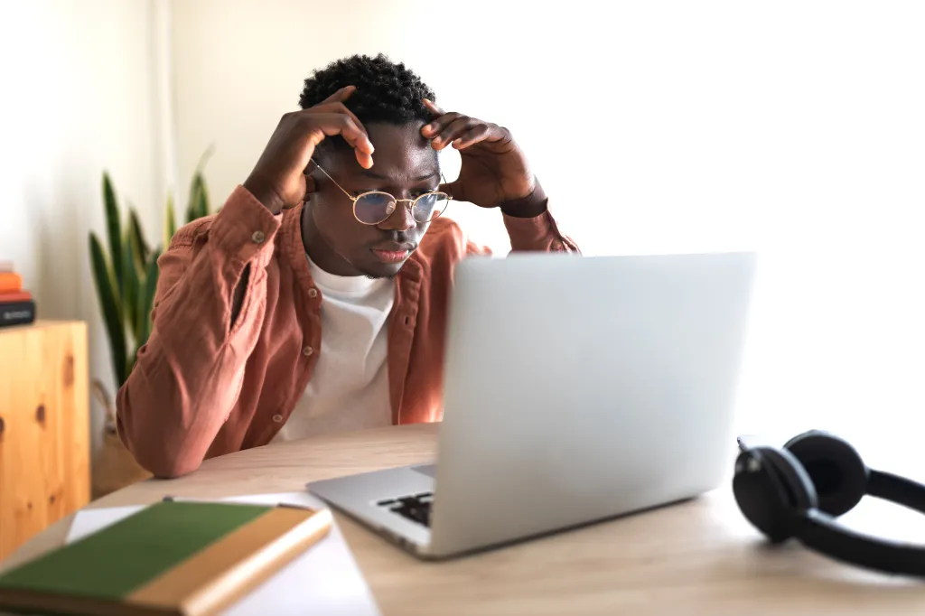 Stressed African American male college student studying in front of a laptop.