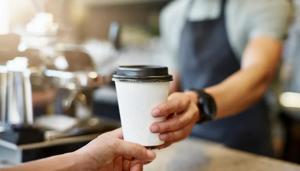Barista handing a coffee to-go cup to a customer.