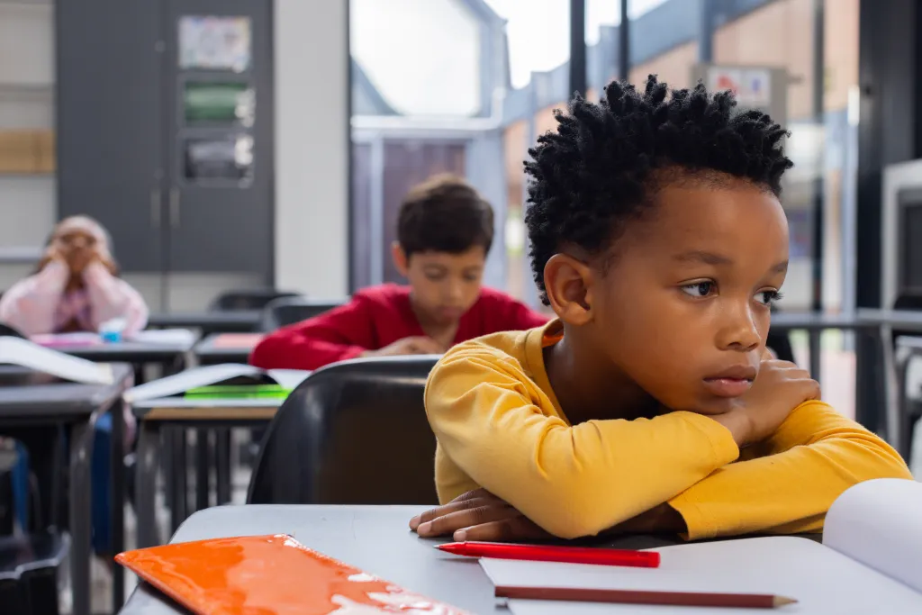 African American boy in a yellow shirt looks sad in a classroom setting with copy space.