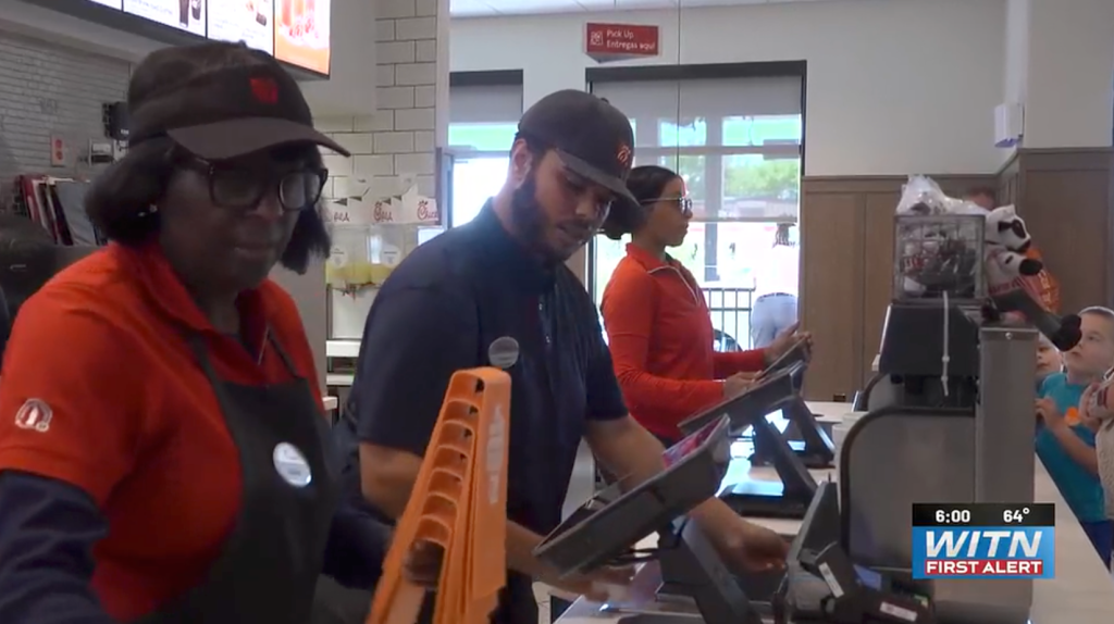 Three Chick-fil-A employees assisting customers at cash registers.