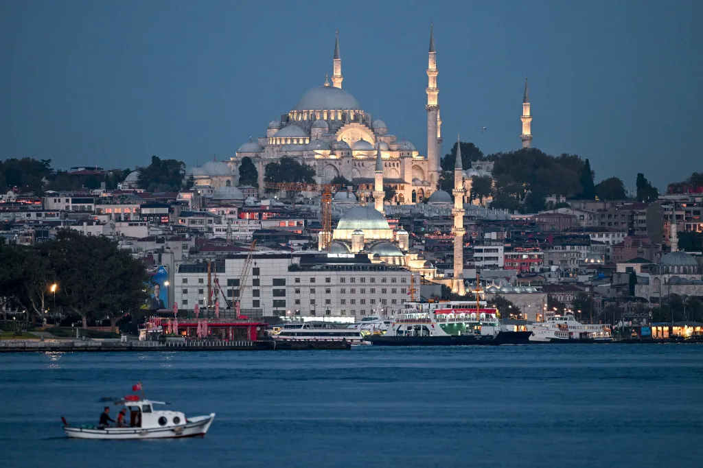 The Süleymaniye Mosque in Istanbul, Turkey, lit up at night, with buildings and boats on the water in the foreground.
