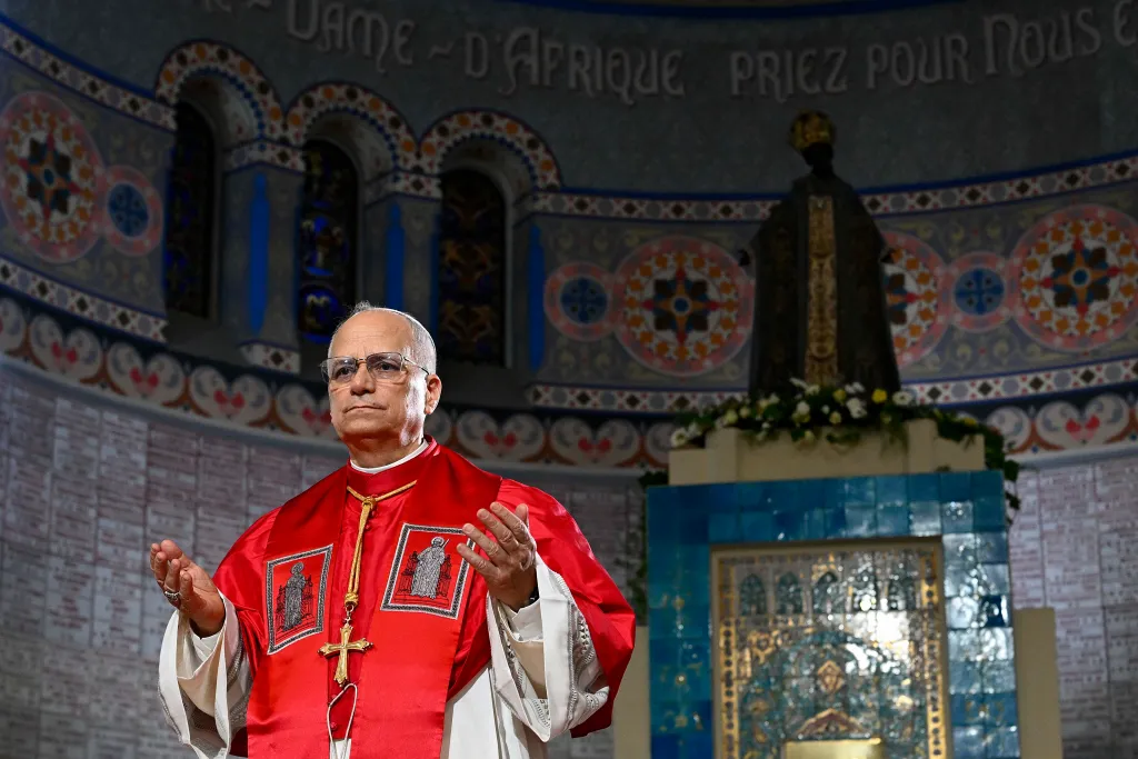 A man in red and white robes, identified as Pope Leo XIV, speaks in a church.
