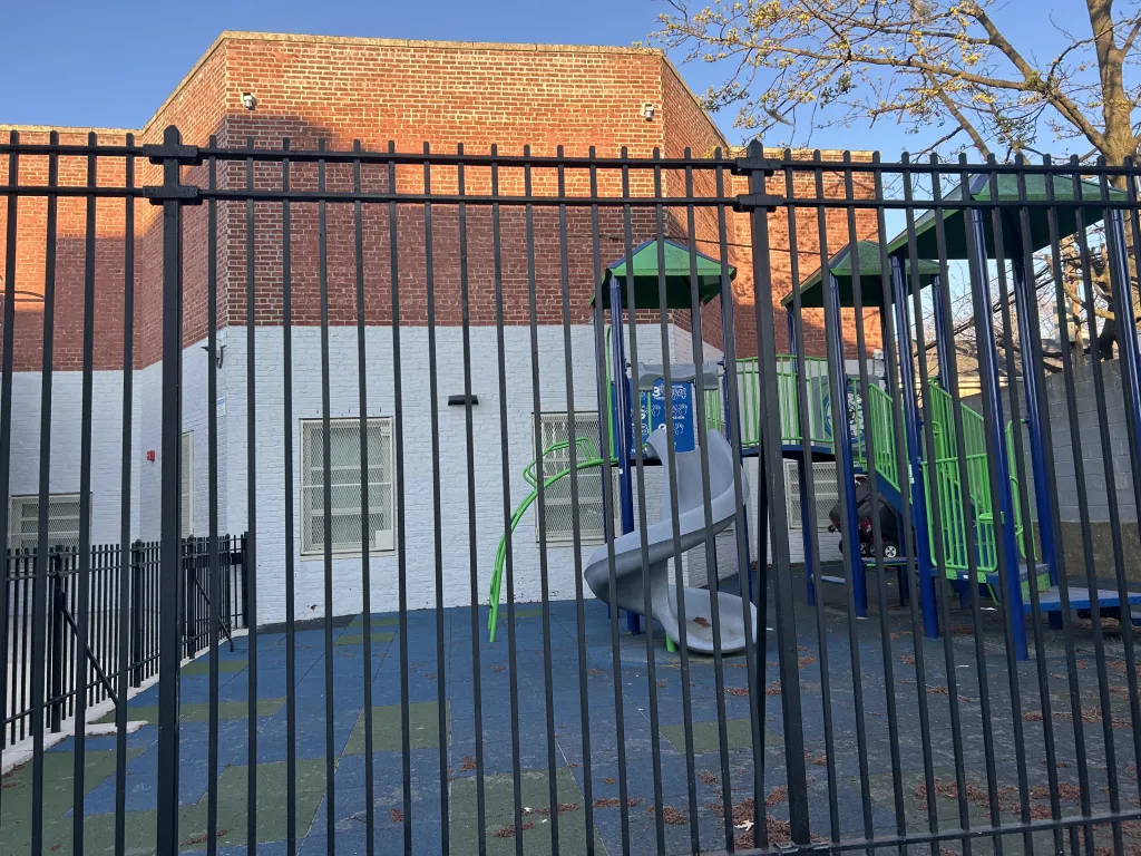 Playground behind a black fence with a brick building in the background.